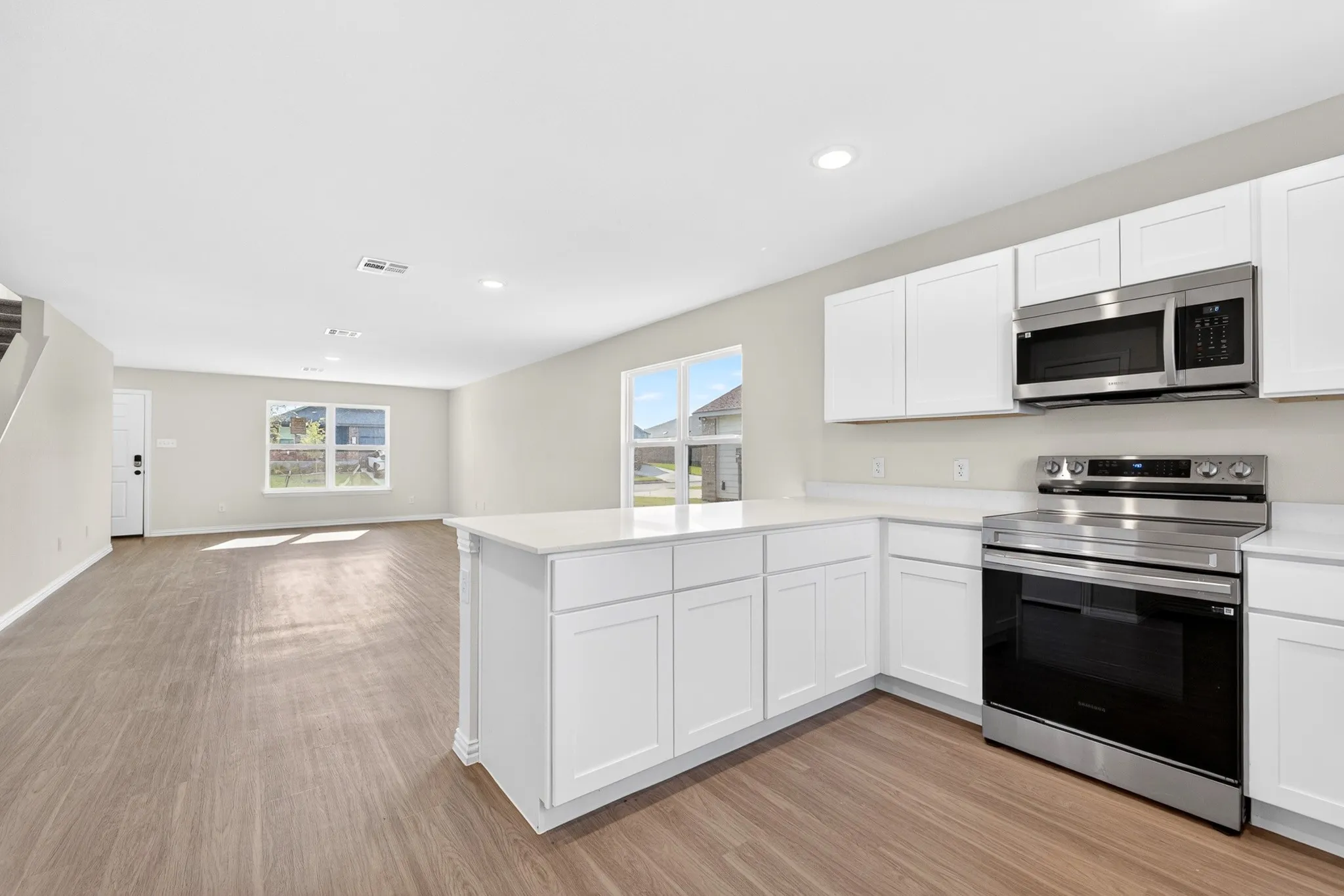 Kitchen island with white shaker cabinetry, white countertops, stainless steel appliances, and wood-finish flooring