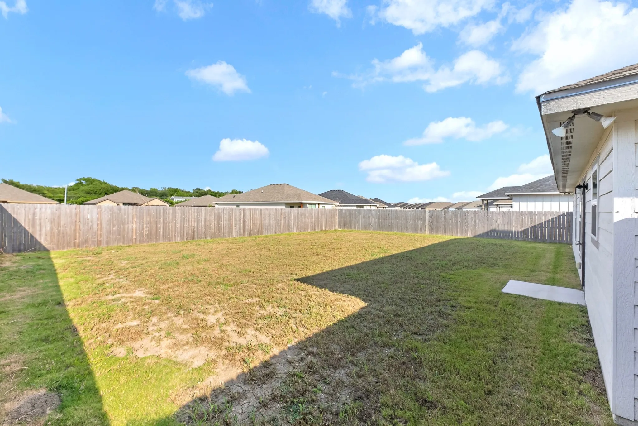 Expansive backyard featuring a natural grass lawn, wood plank fencing, and a concrete paver path