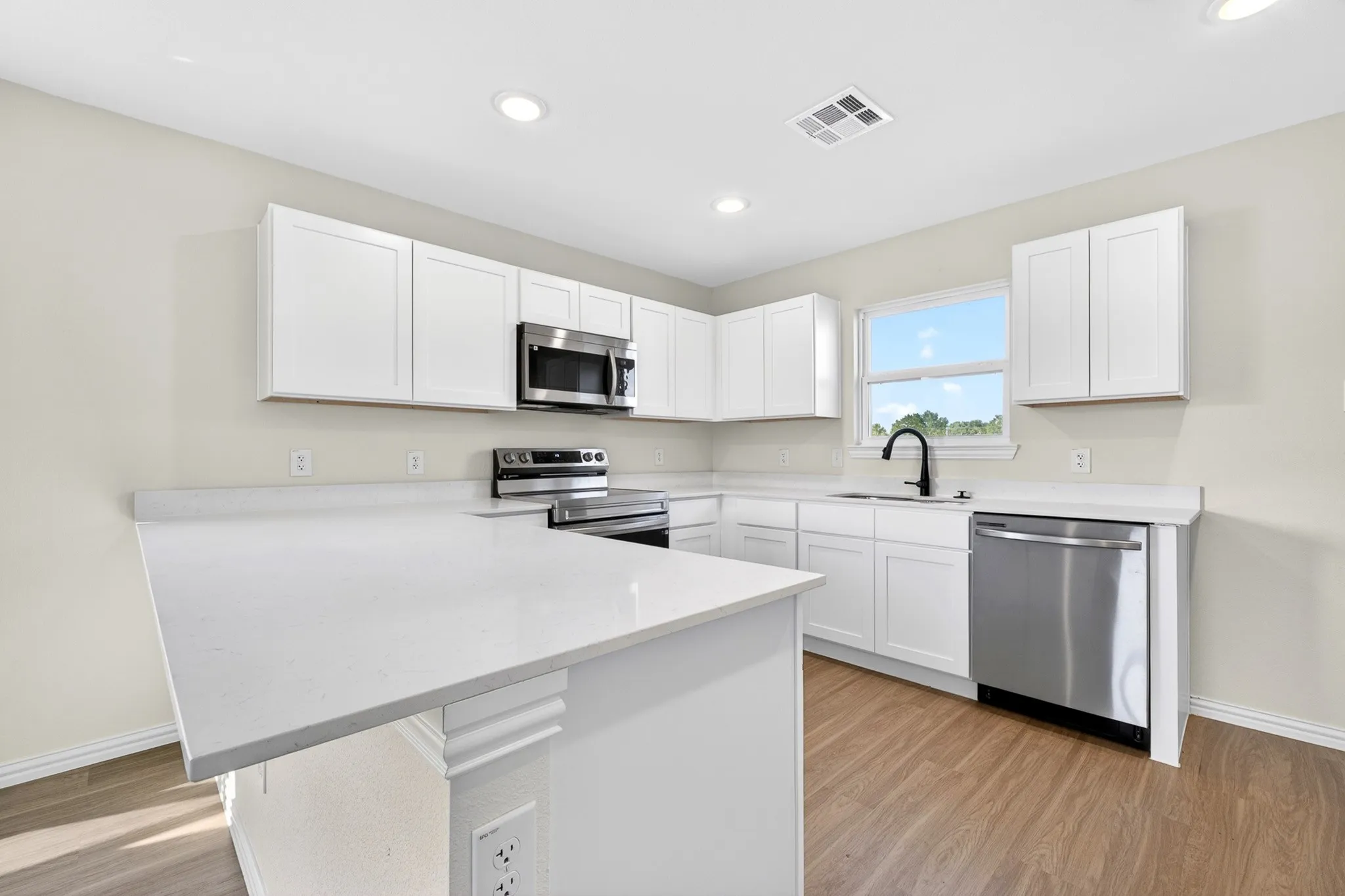Kitchen featuring white cabinetry, light-toned countertops, stainless steel appliances, wood-finish flooring, and recessed lighting