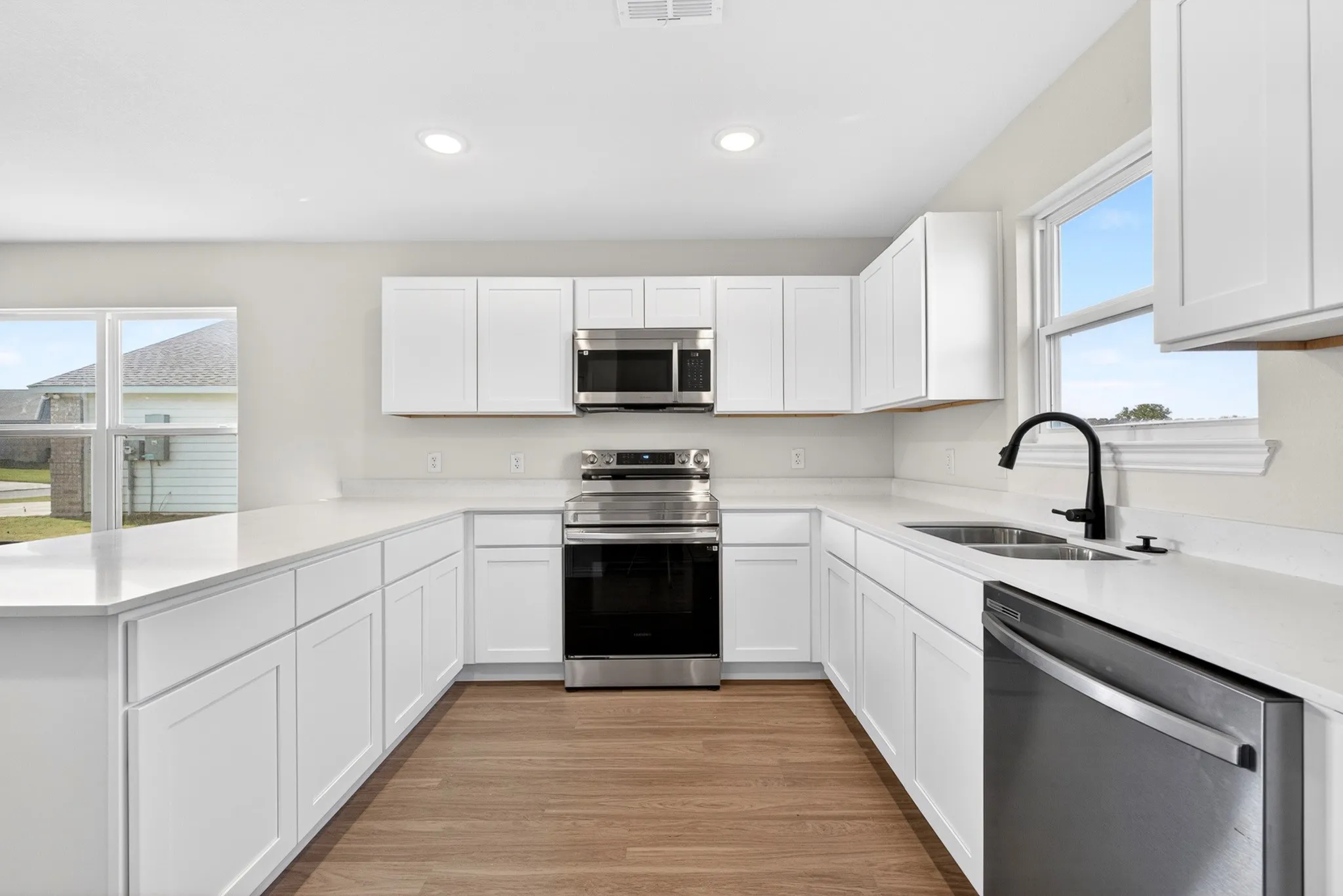 Bright kitchen featuring white shaker cabinetry, stainless steel appliances, light countertops, and wood-finish flooring