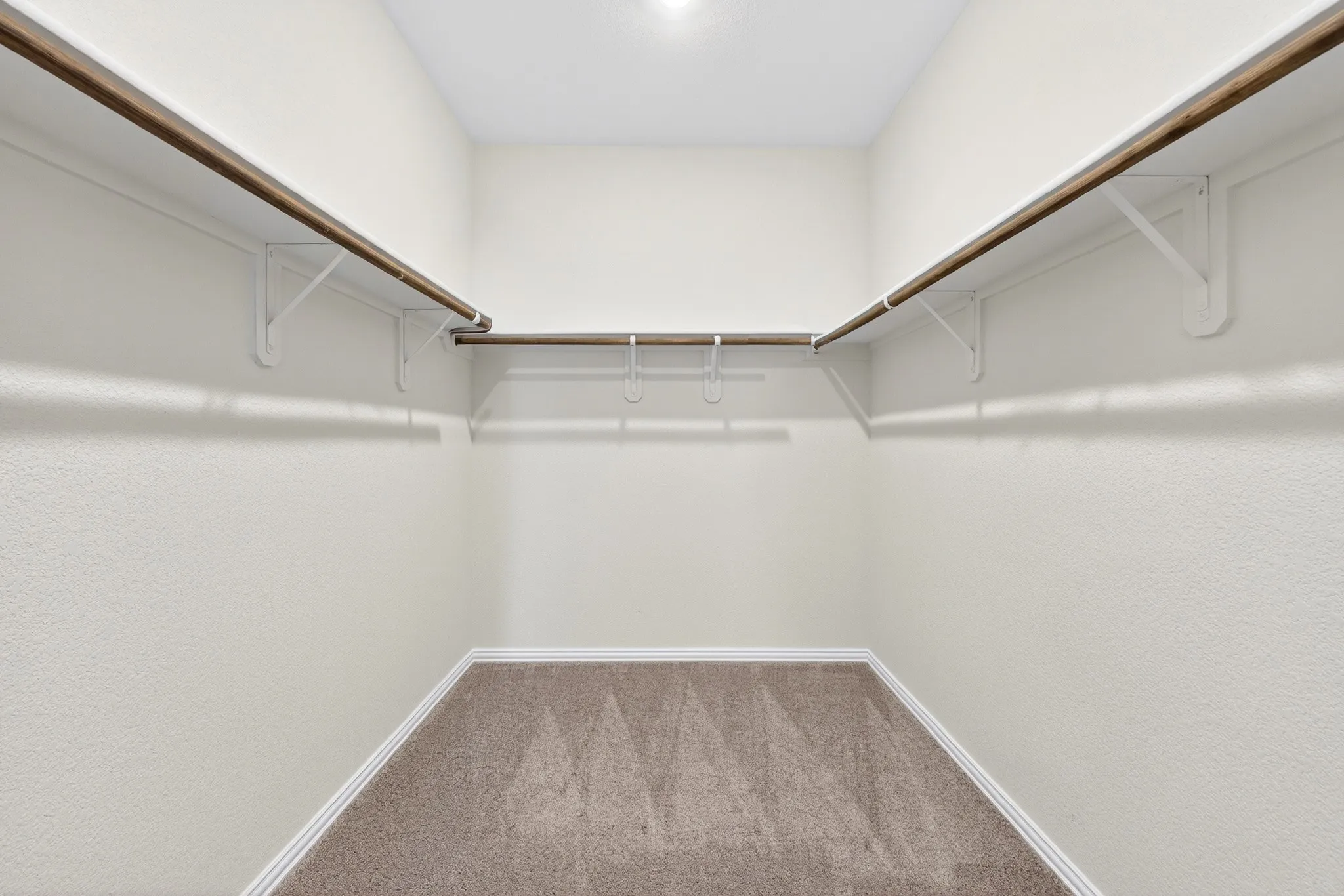 Spacious walk-in closet featuring dual clothing rods, abundant shelving, carpet flooring, and recessed ceiling lighting for optimal organization and visibility