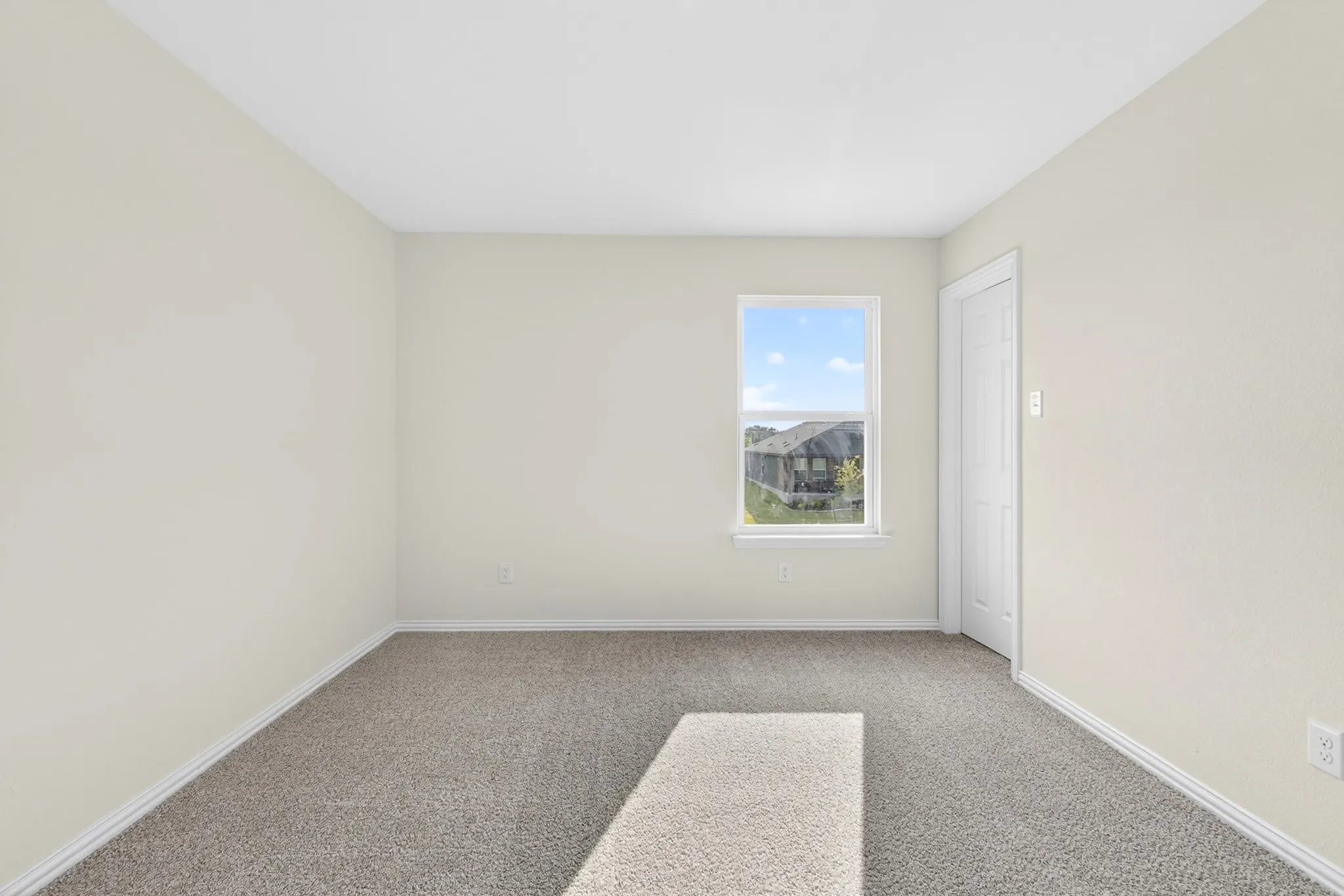 Neutral wall color, light gray carpet, single window with white trim, white interior door, white ceiling