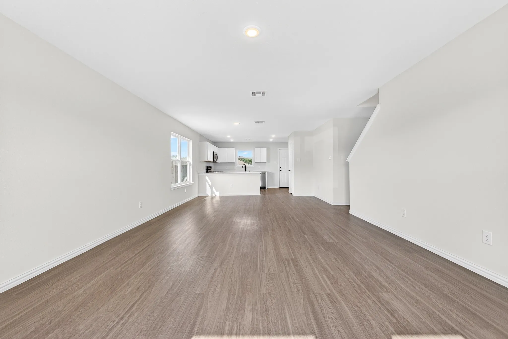 Open-concept living area featuring wood-finish flooring, recessed lighting, and a kitchen with an island, white cabinetry, and stainless-steel appliances