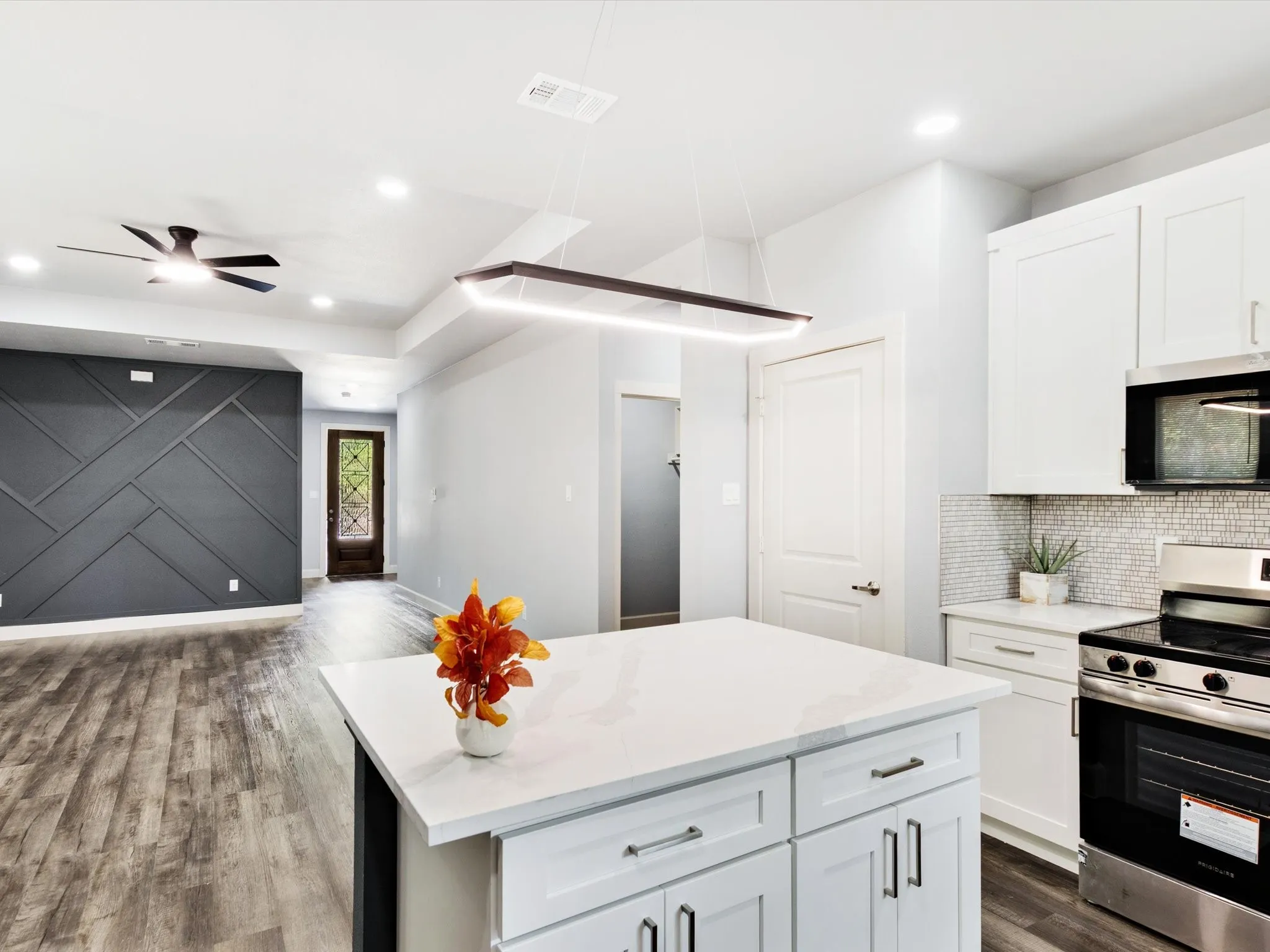 Open-concept kitchen featuring an island with a light-toned countertop, white cabinetry with dark hardware, and a tile backsplash