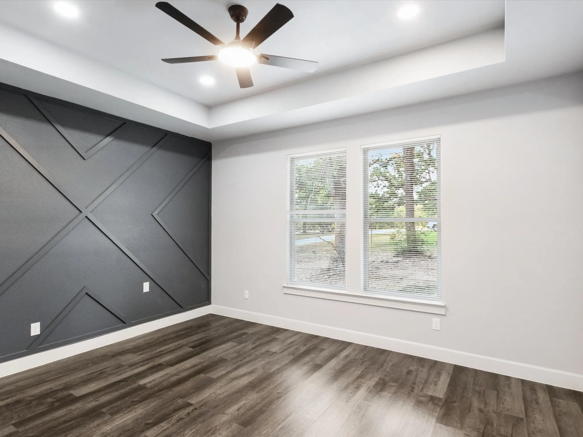 Tray ceiling with recessed lighting, dark accent wall with geometric millwork, wood-finish flooring, and a ceiling fan with integrated lighting