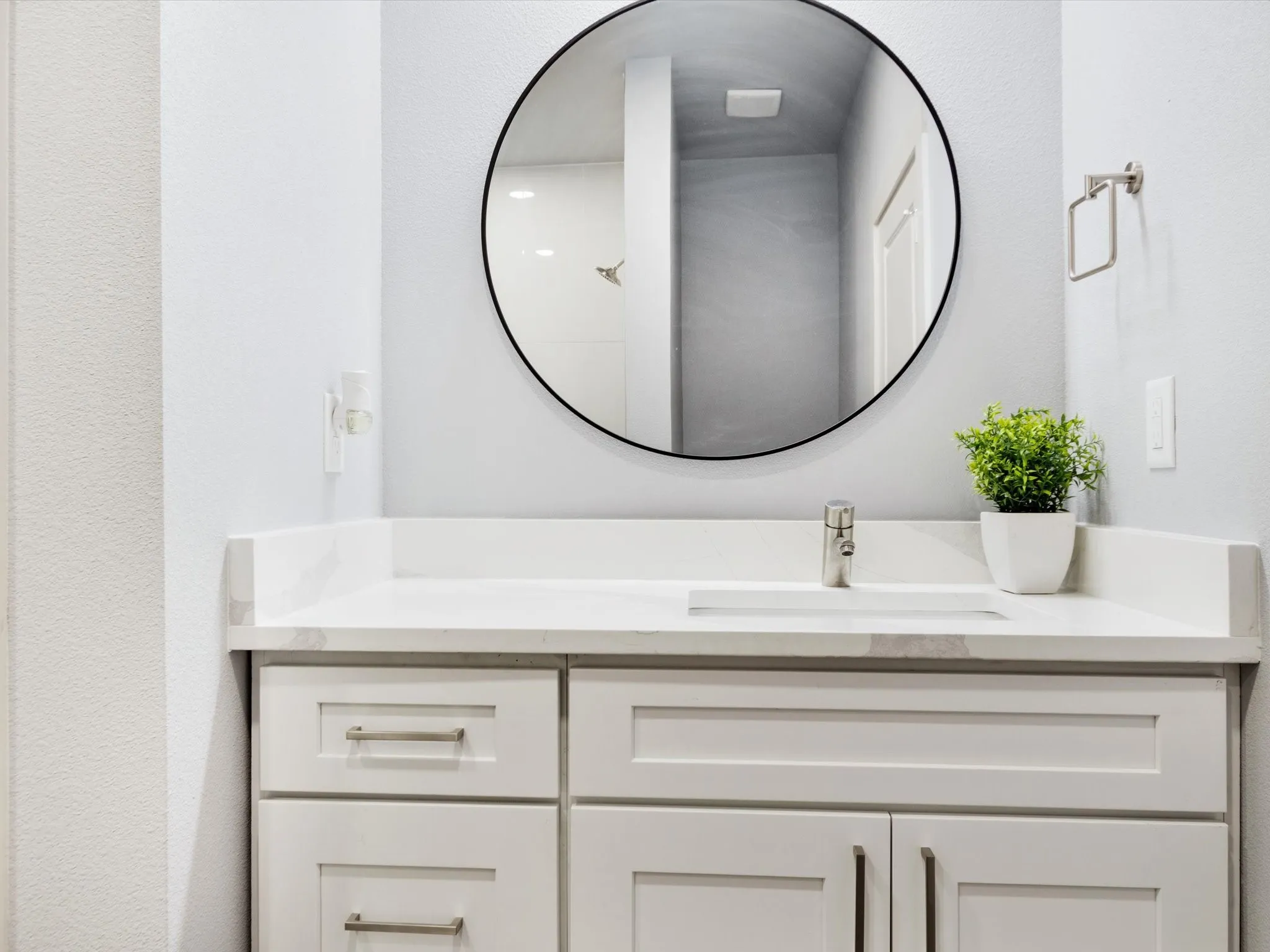 White shaker-style vanity with brushed nickel hardware, integrated rectangular sink, single-handle faucet, and round black-framed mirror