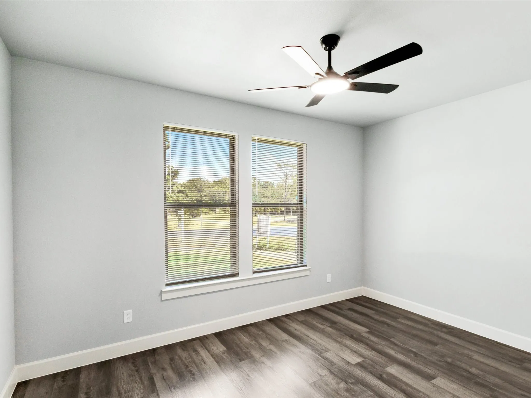 Dual windows with horizontal blinds, wood-finish flooring, and a ceiling fan with integrated lighting