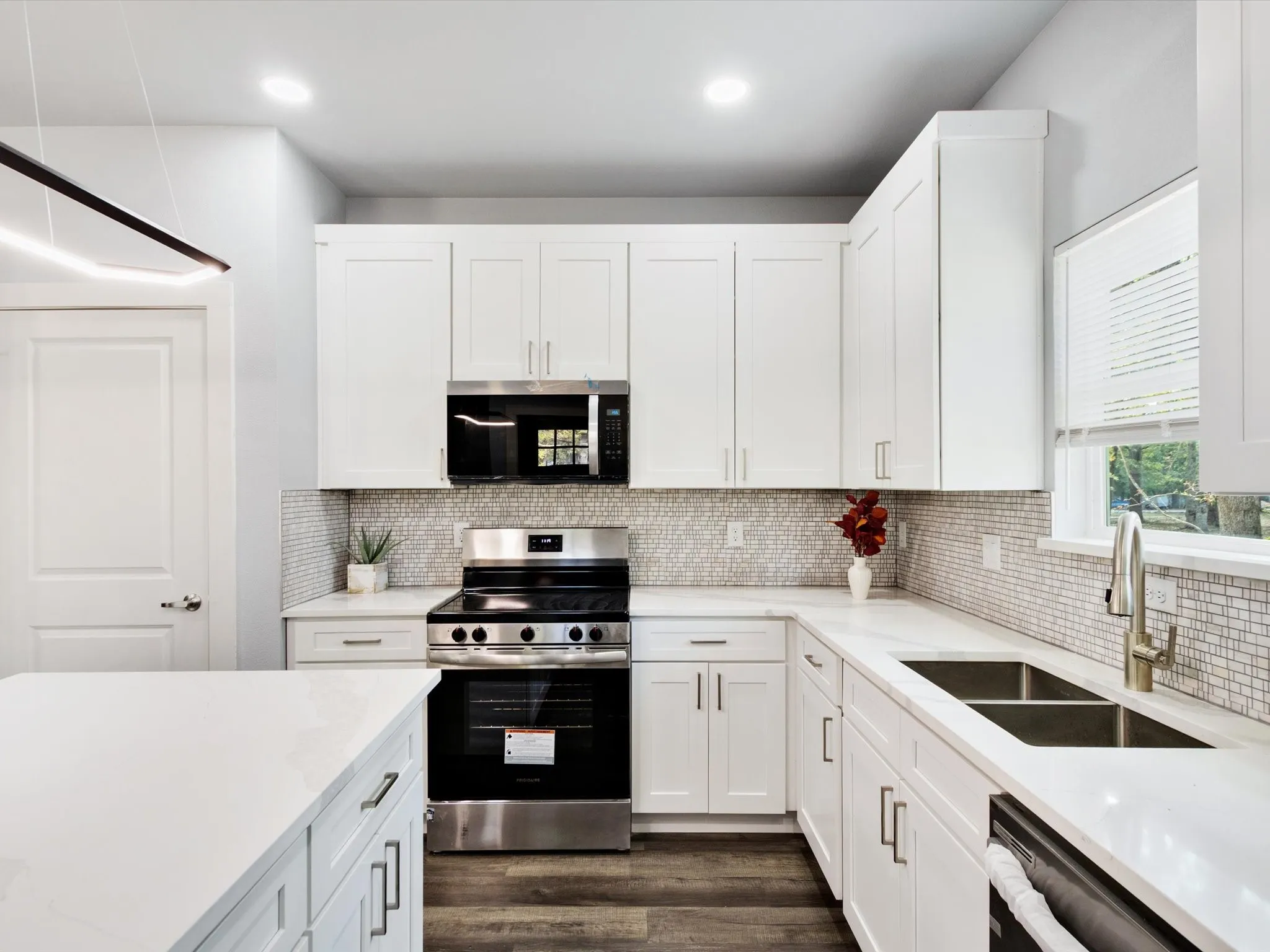 Modern kitchen featuring white shaker cabinetry, stainless steel appliances, quartz countertops, and a mosaic tile backsplash