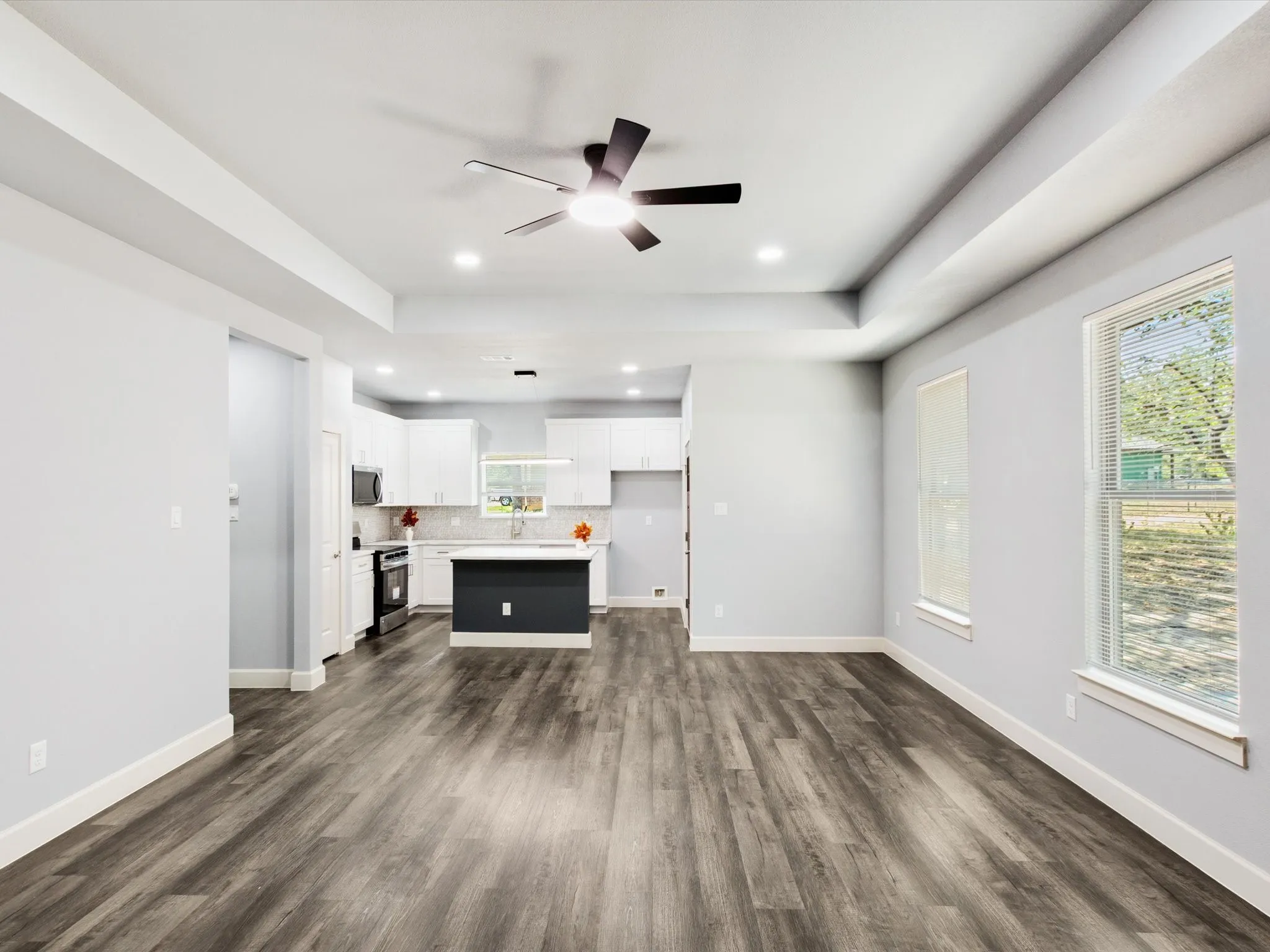 Tray ceiling with recessed lighting and a ceiling fan, wood-finish flooring, white cabinetry, dark kitchen island, and multiple windows