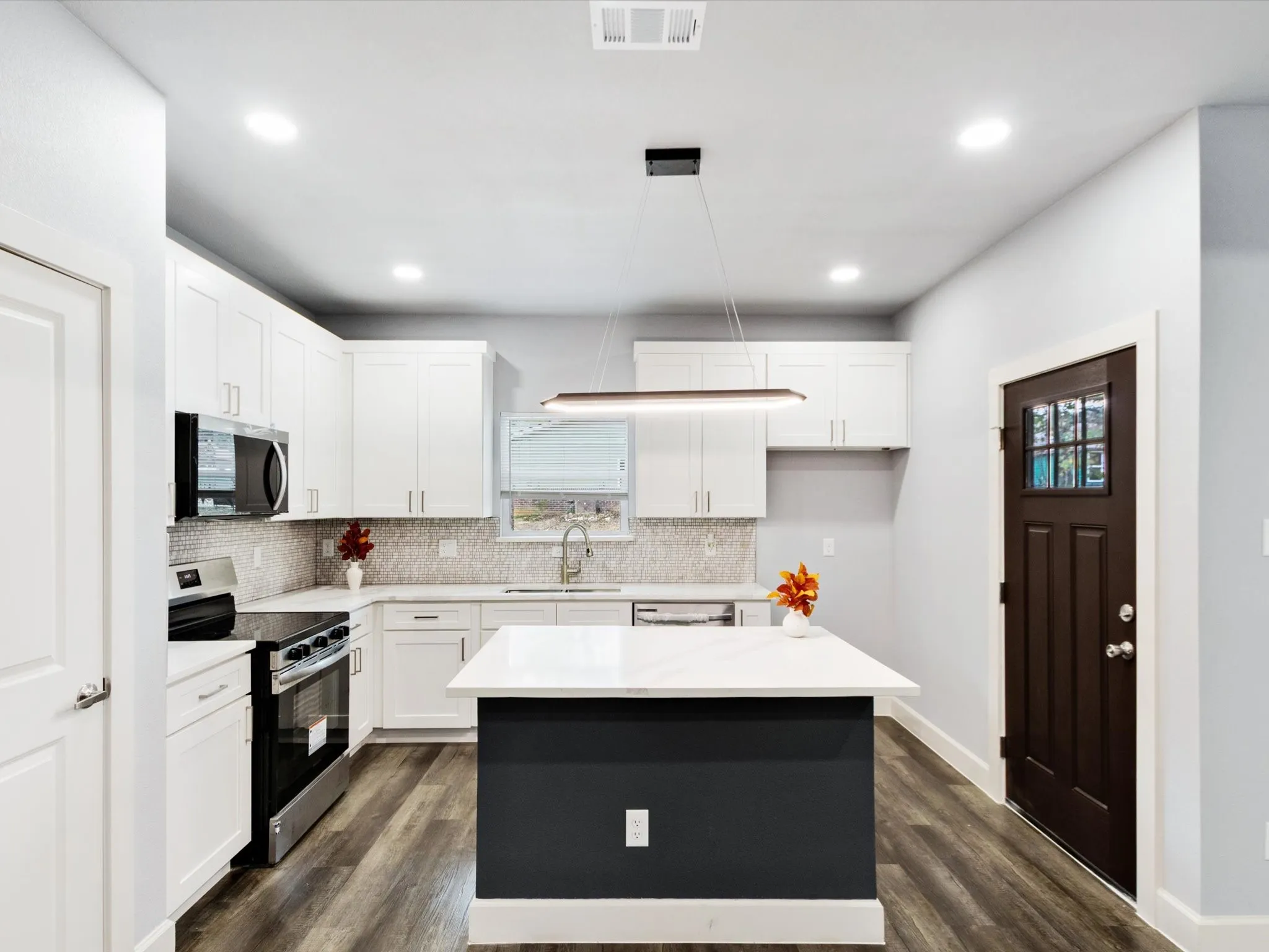 Modern kitchen featuring white cabinetry, stainless steel appliances, a center island with a light countertop, wood-finish flooring, and a decorative tile backsplash