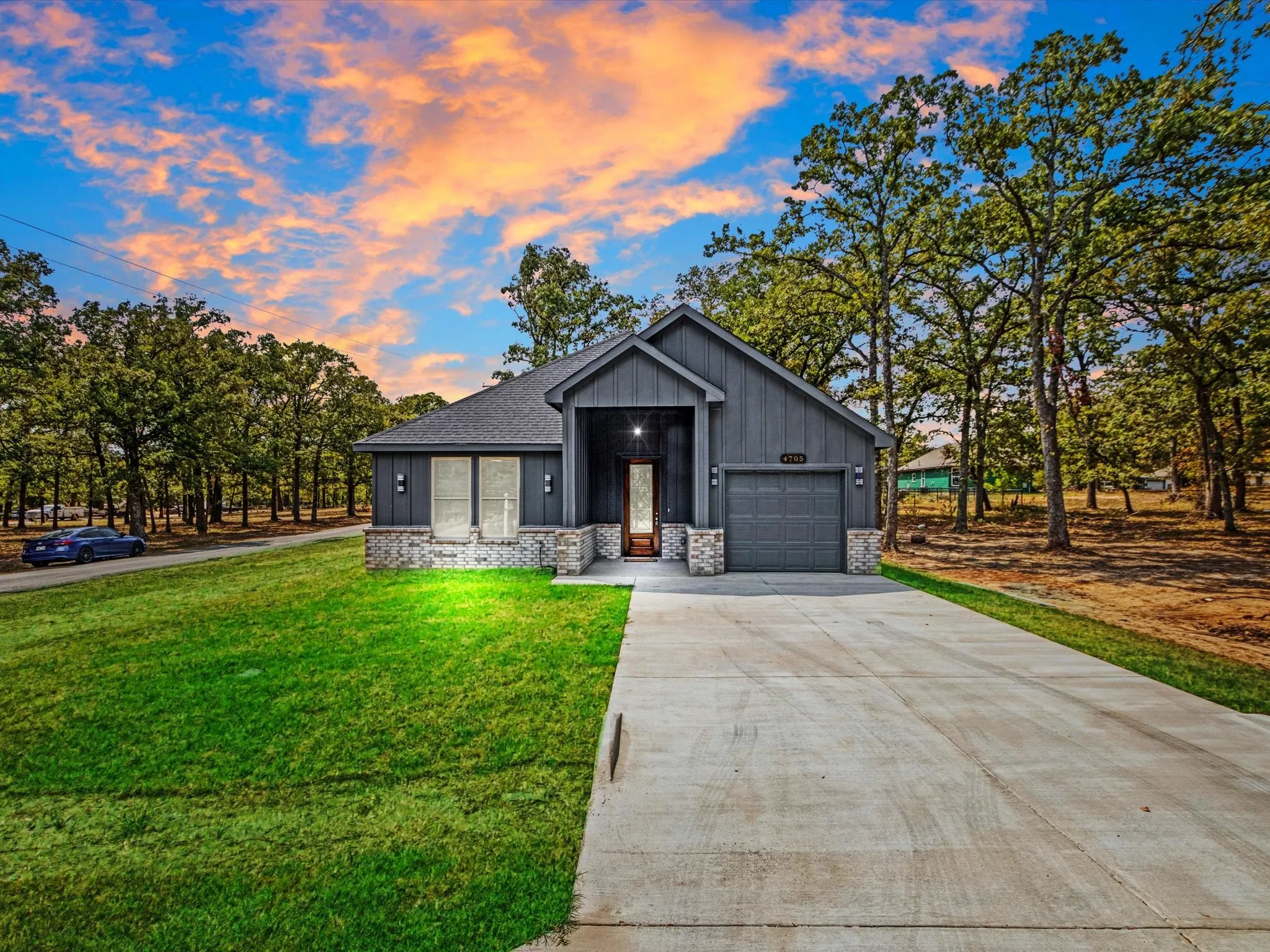 Contemporary exterior with dark vertical siding, stone accents, attached garage, and a concrete driveway