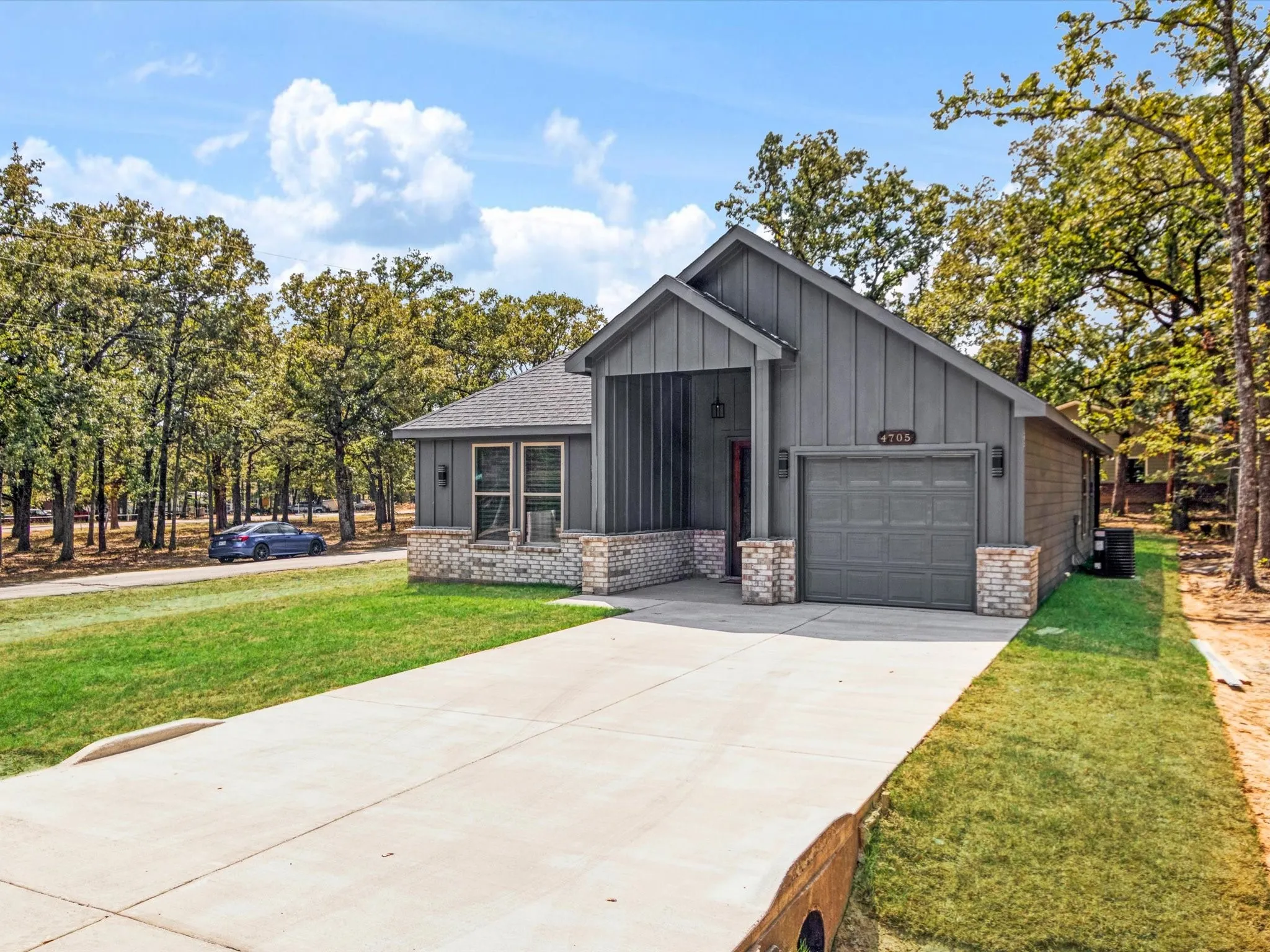 Contemporary exterior with vertical panel siding, brick accents, an attached garage, a concrete driveway, and established trees