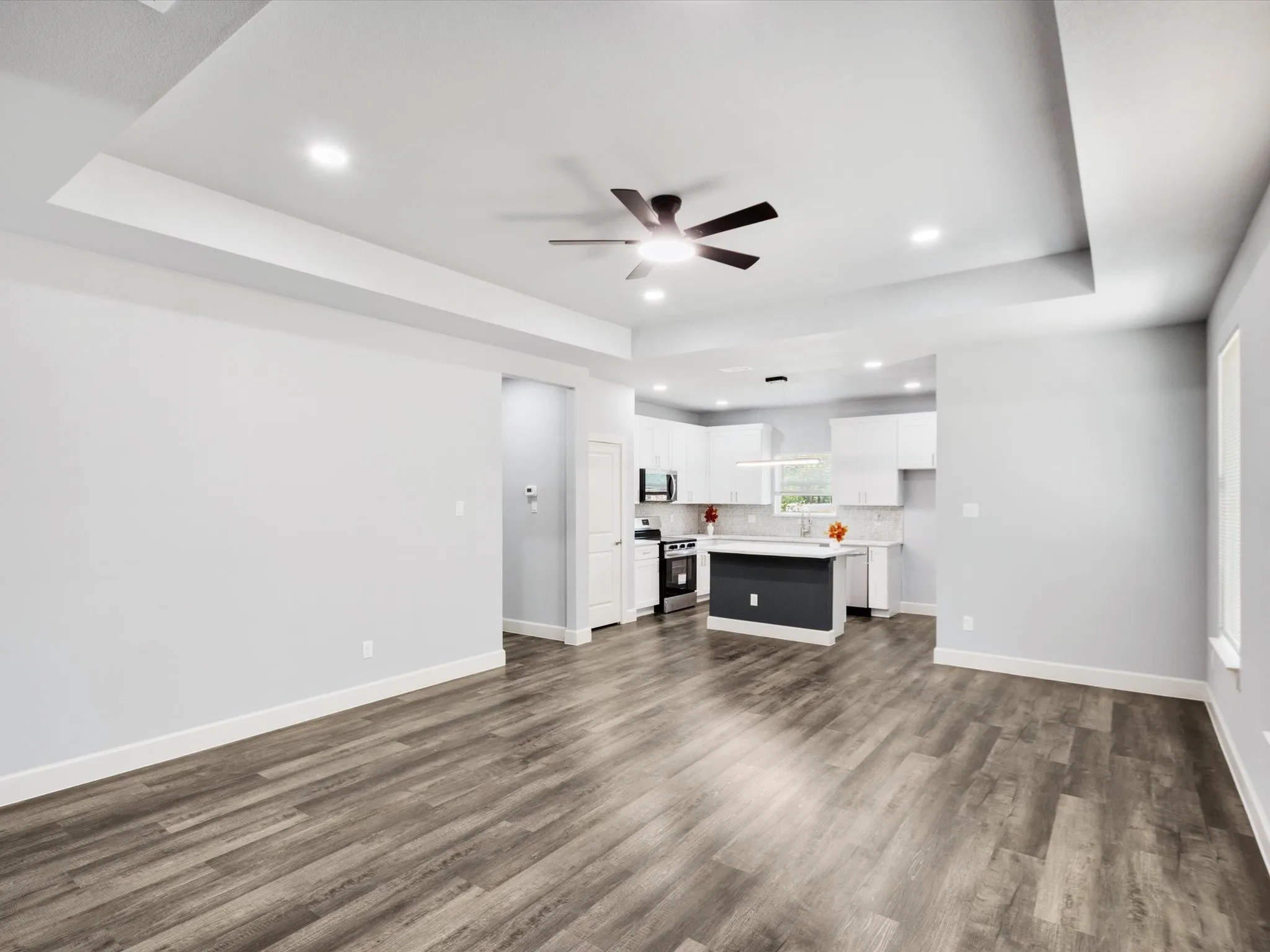 Tray ceiling with recessed lighting, ceiling fan, wood-finish flooring, white cabinetry, and a kitchen island with a dark base