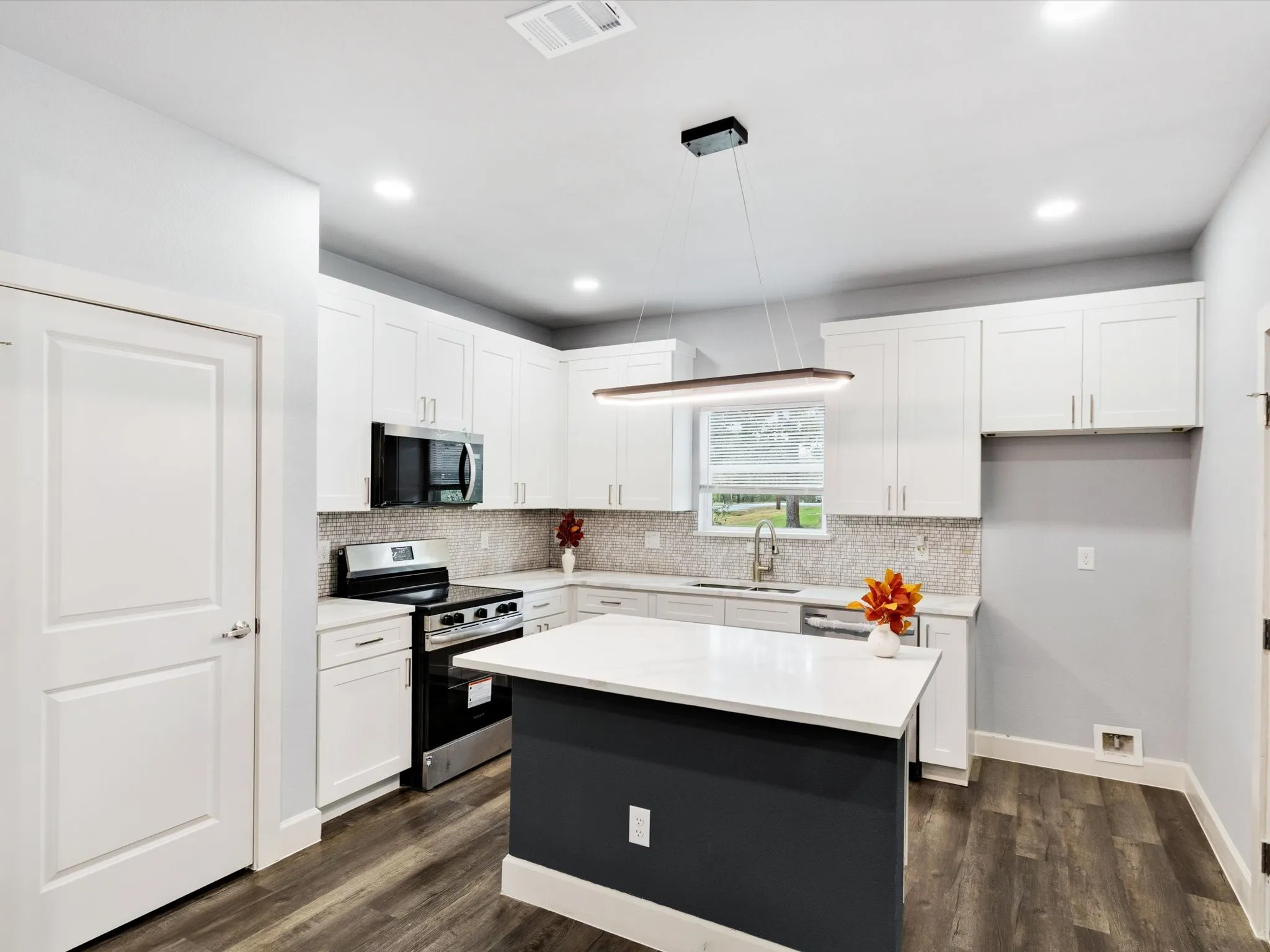 Modern kitchen featuring white shaker cabinetry, stainless steel appliances, a center island with a light-colored countertop, and wood-finish flooring