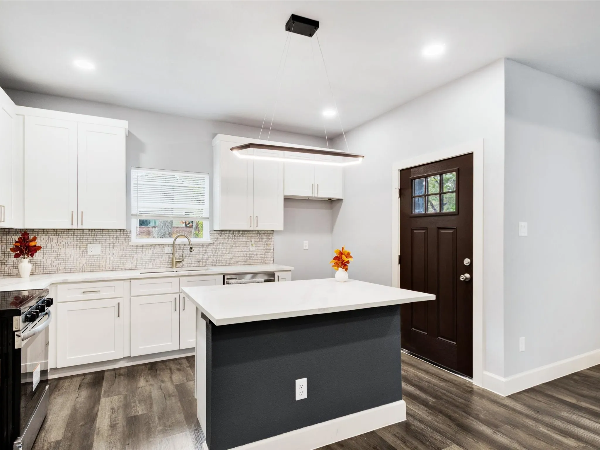 Modern kitchen featuring white shaker cabinetry, an island with a white countertop, wood-finish flooring, a mosaic tile backsplash, and recessed lighting