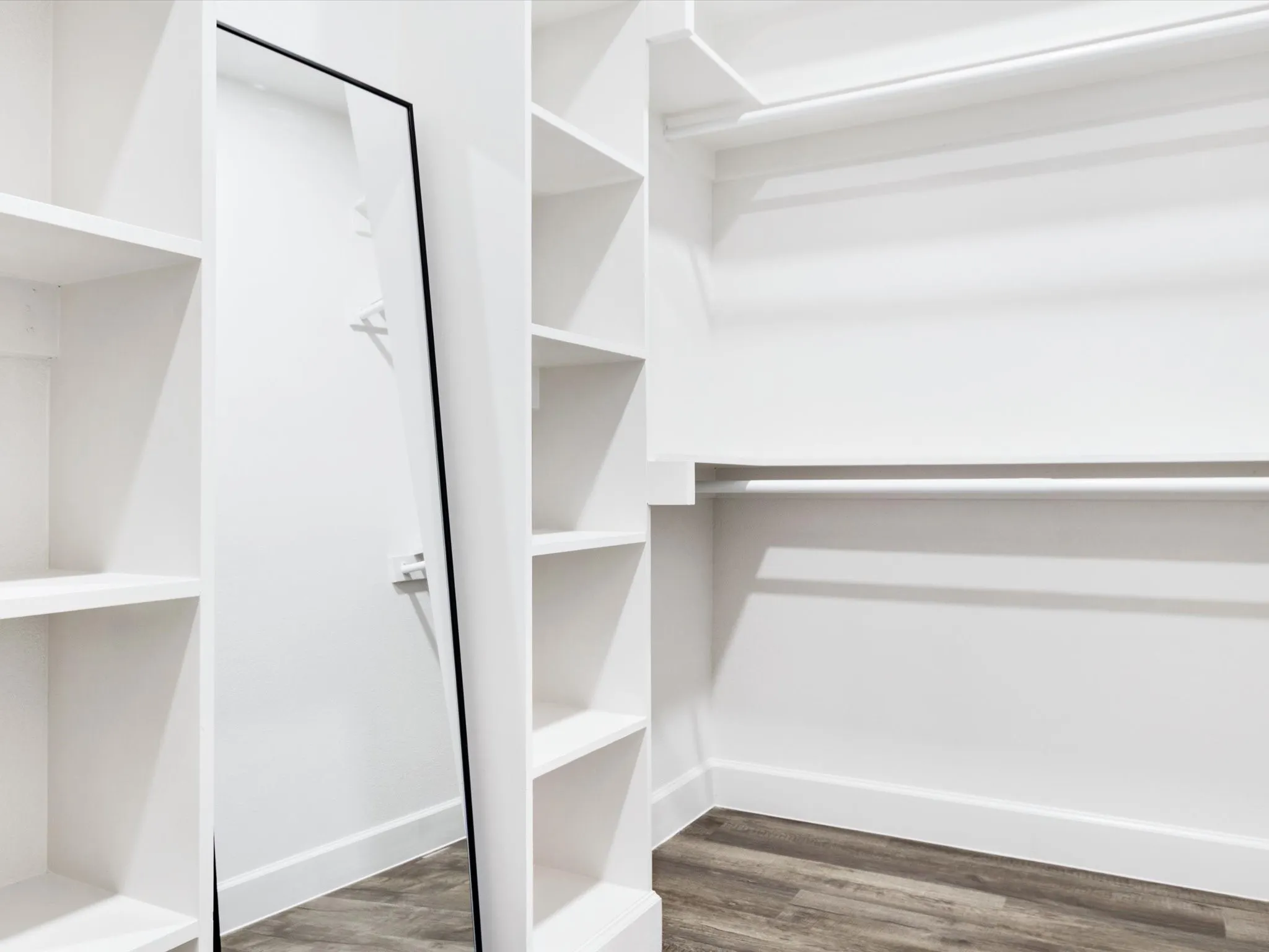 Built-in shelving, hanging rods, full-length mirror, wood-finish flooring, and white trim