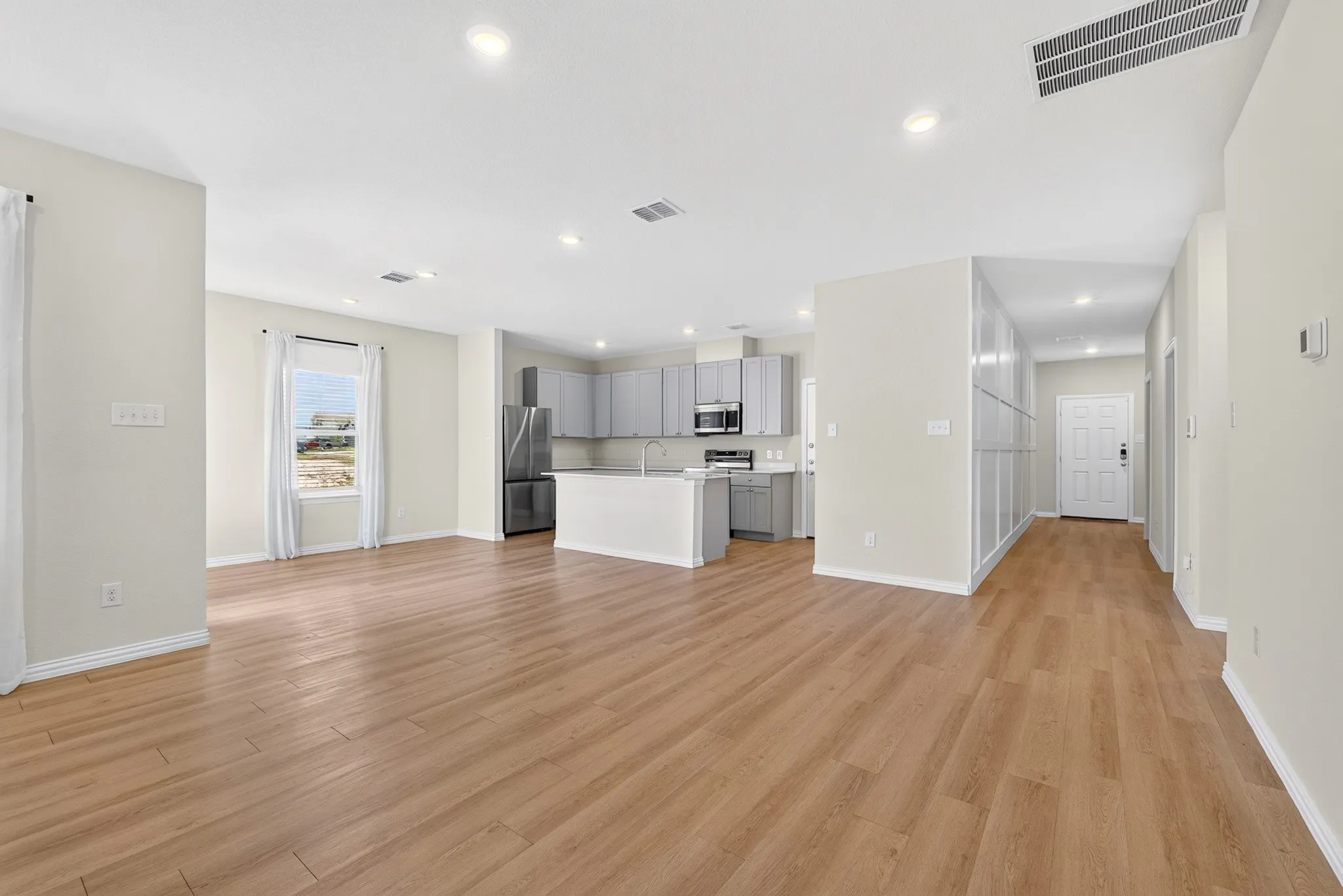 Open-concept living space featuring wood-finish flooring, recessed lighting, a kitchen island, stainless steel appliances, and light-toned cabinetry