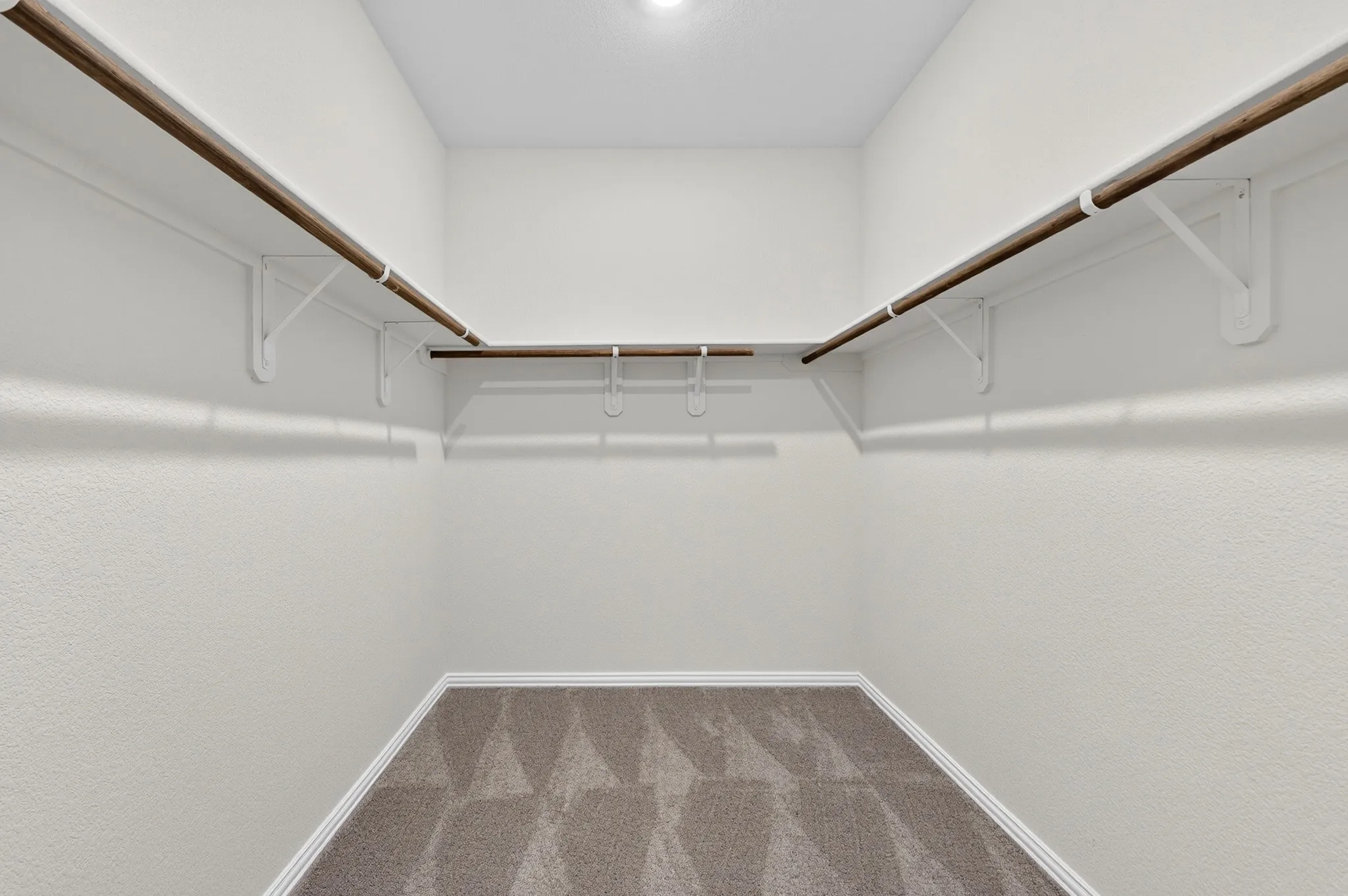 Wall-to-wall carpeting with geometric pattern, white walls, wood-finish hanging rods, and white shelving brackets