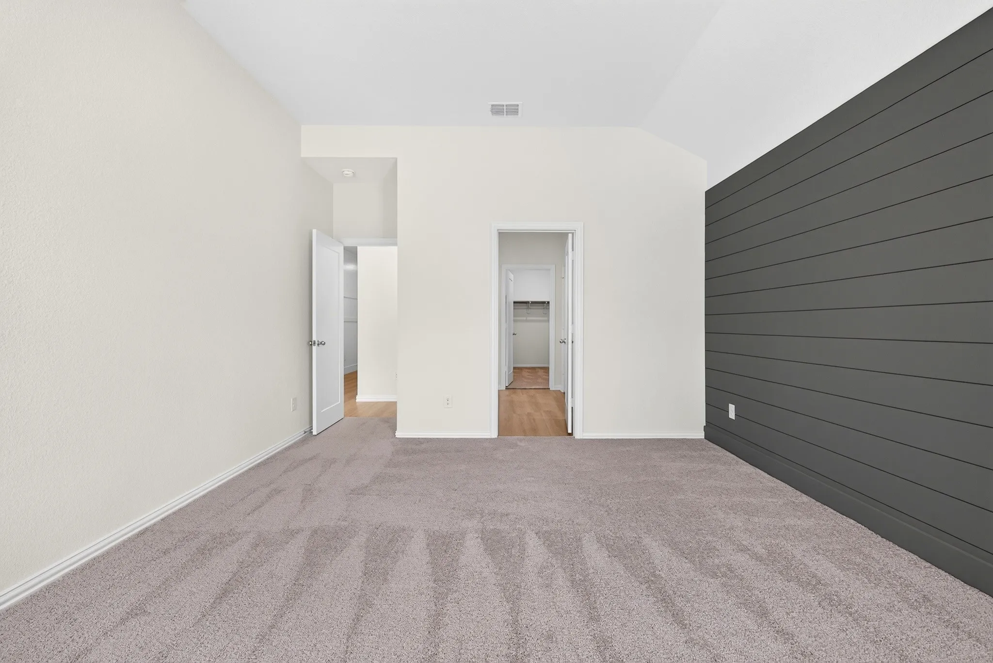 Neutral-toned wall finishes, vaulted ceiling, and plush gray carpeting