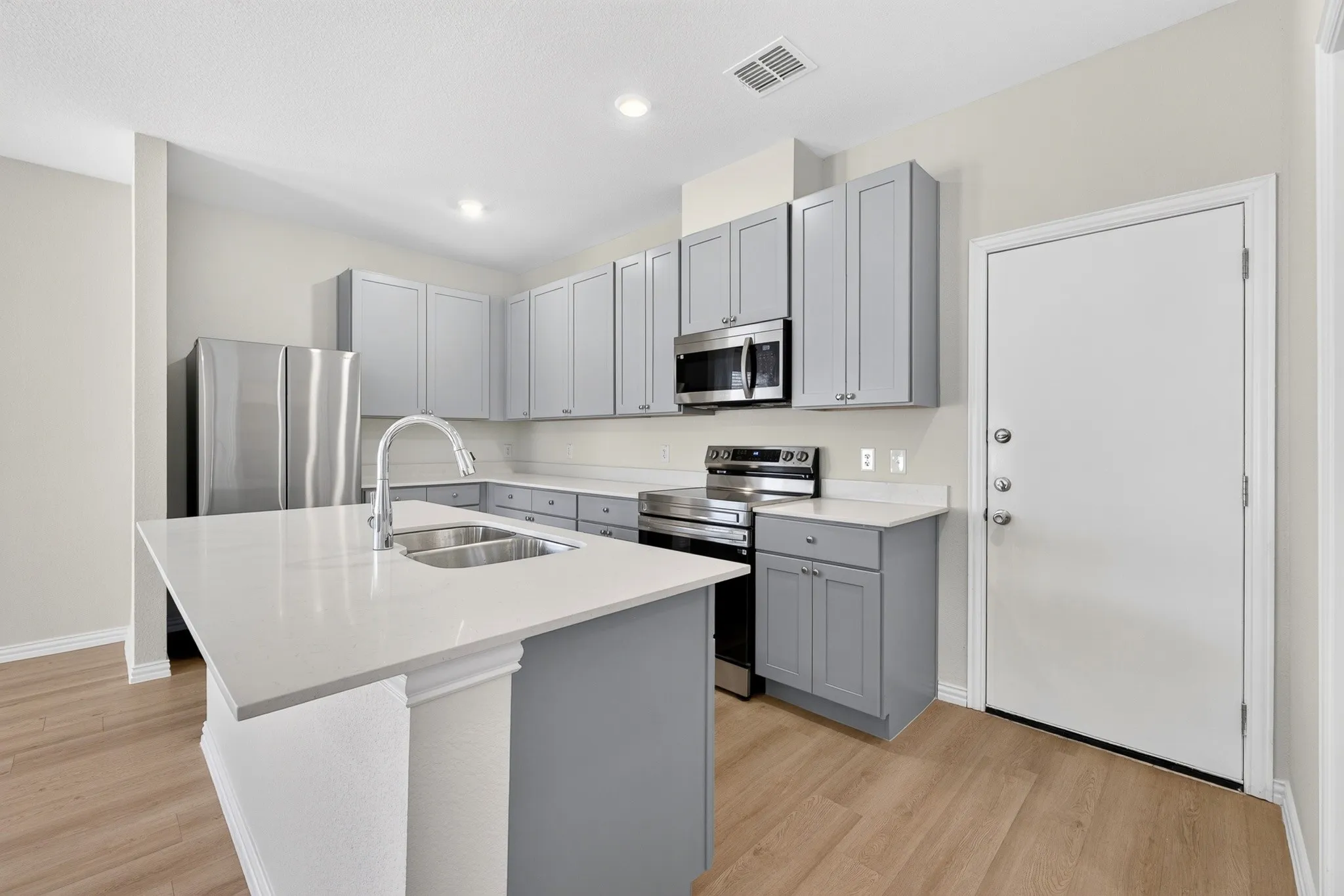 Kitchen featuring a large central island, stainless steel appliances, gray cabinetry, light-toned countertops, and wood-finish flooring