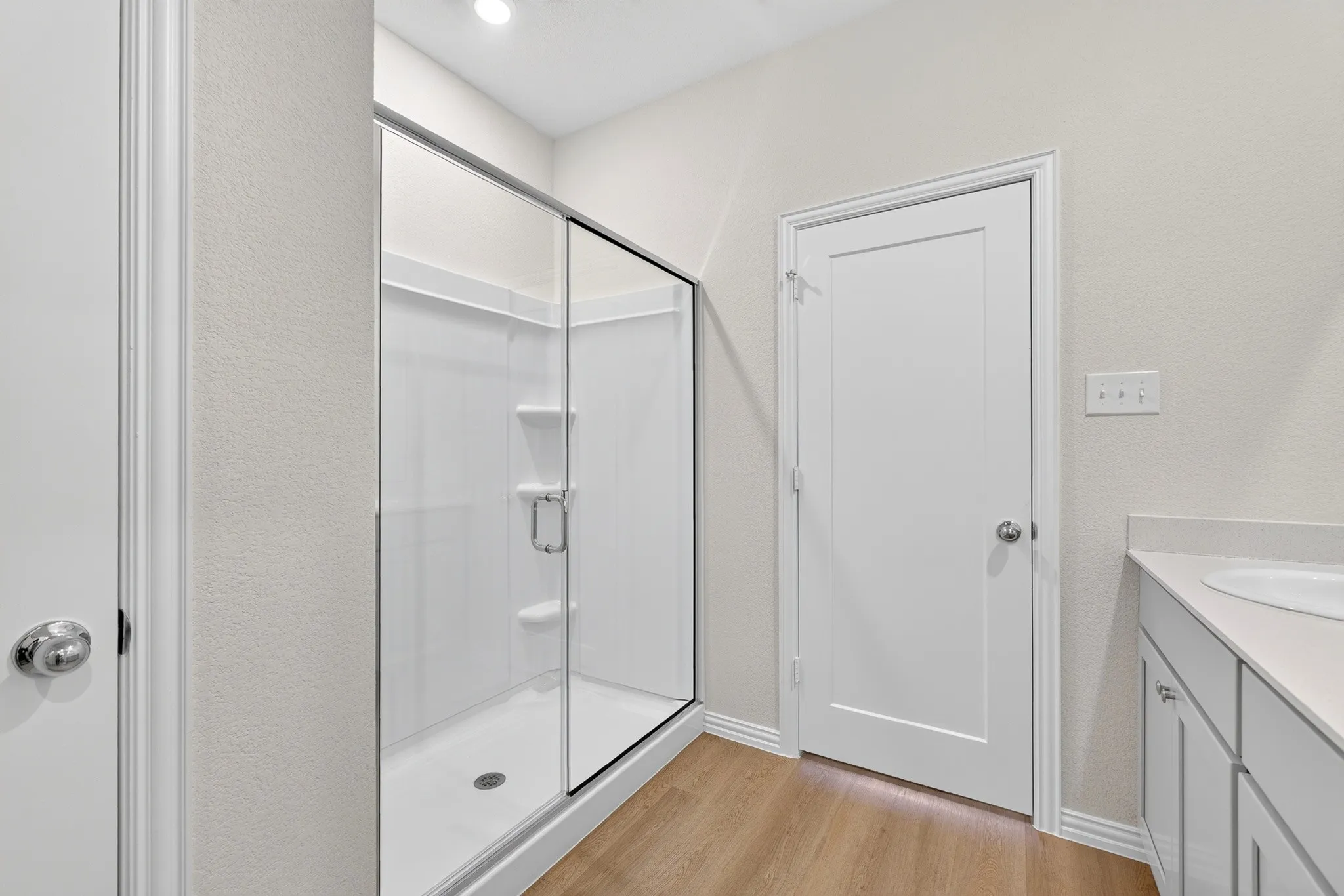 Glass-enclosed shower with built-in shelving, wood-finish flooring, and a vanity with an integrated sink and base cabinetry