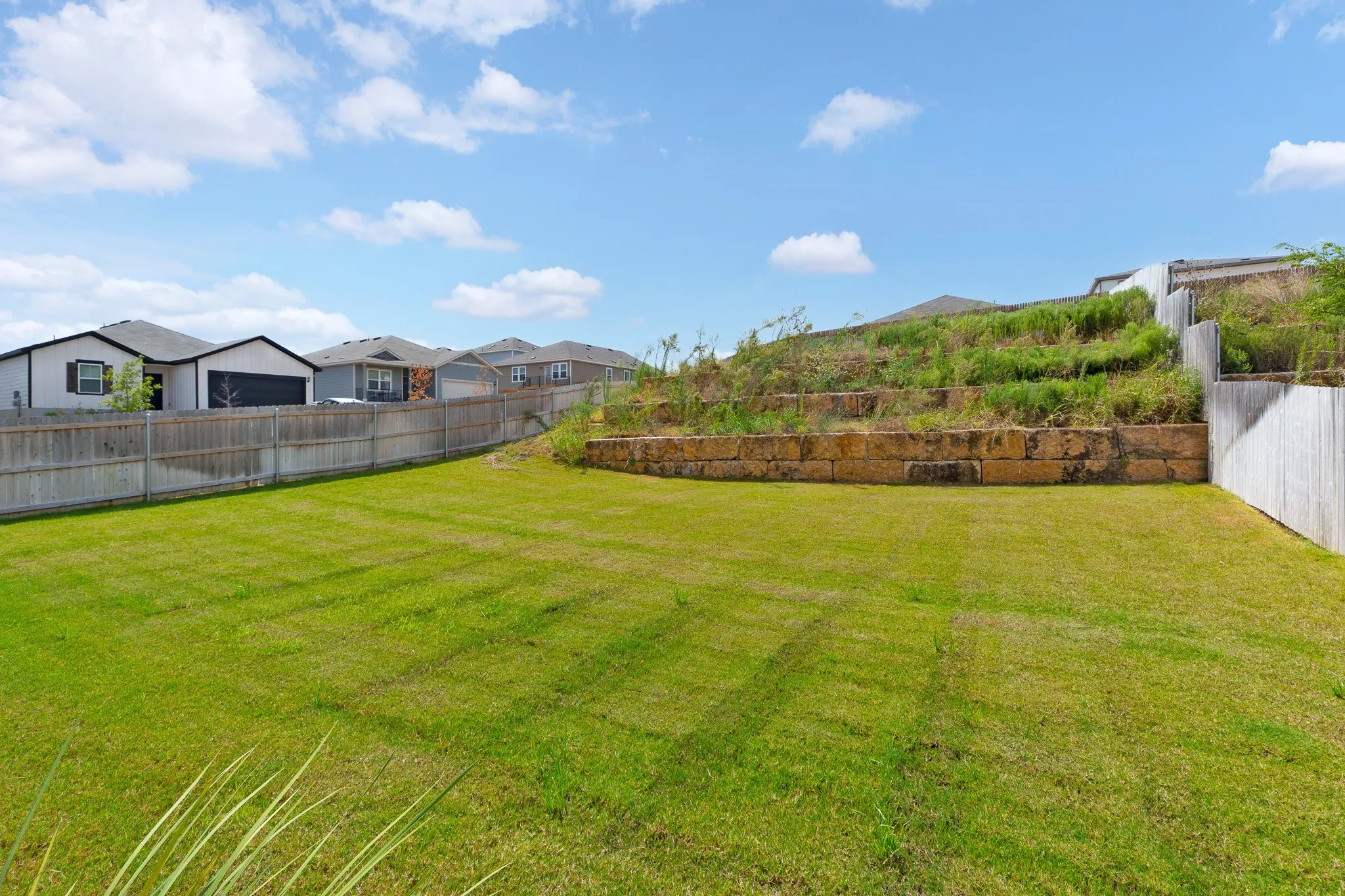 Expansive grass lawn with wood fencing and a stone retaining wall