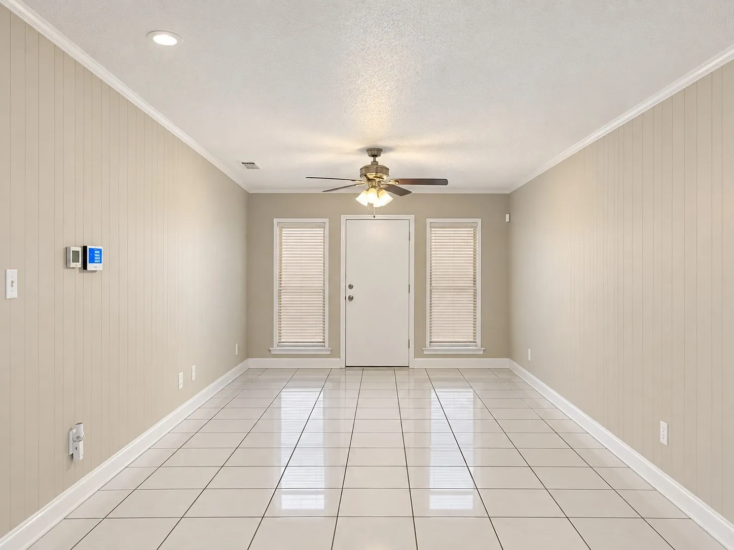 Light-toned tile flooring, panel walls, ceiling fan with light, and two windows with blinds