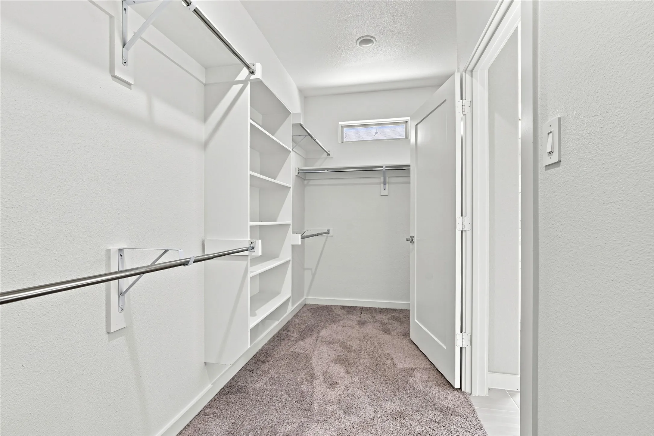 Walk-in closet featuring built-in shelving, chrome hanging rods, recessed ceiling lighting, and a transom window