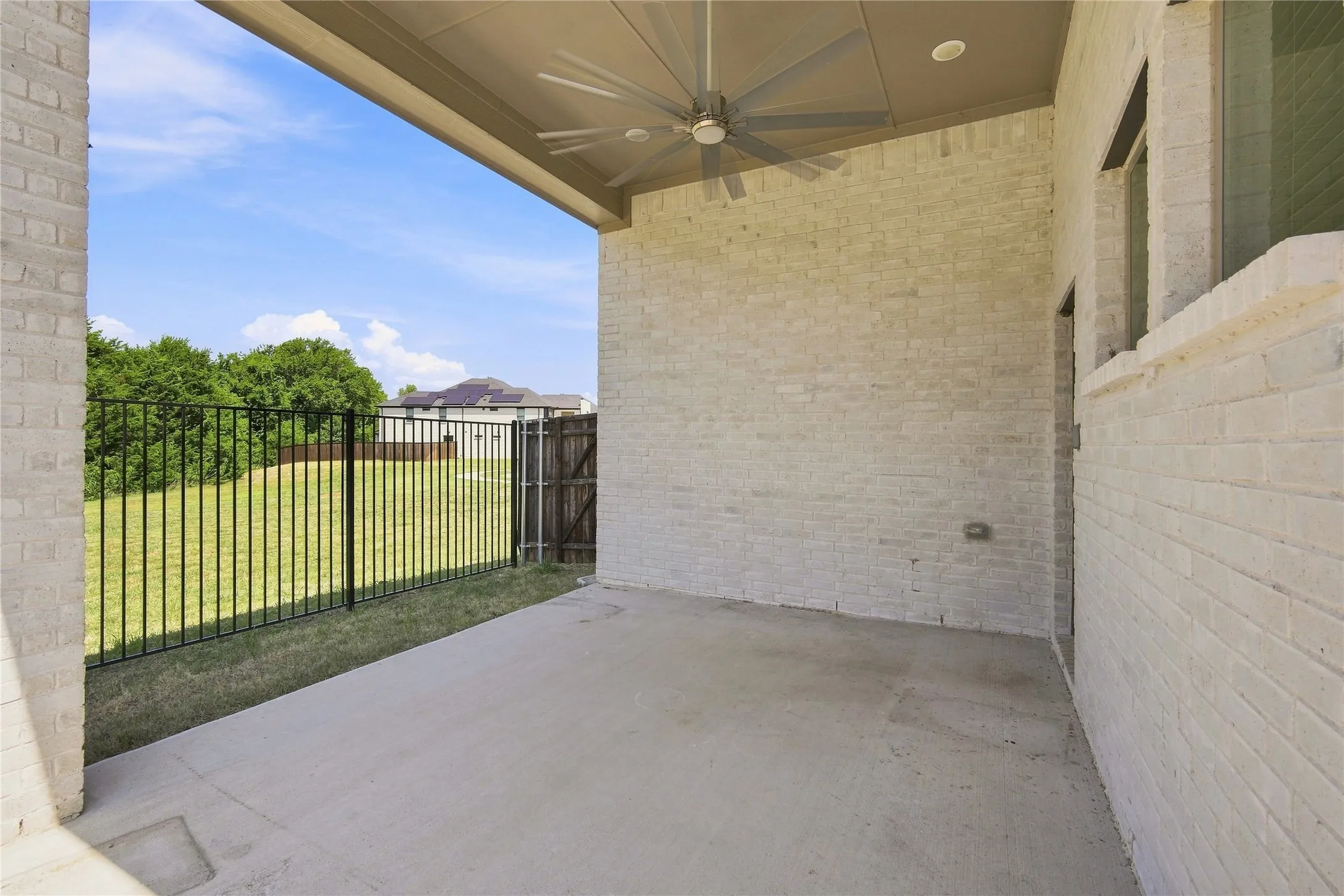 Covered outdoor patio with a concrete surface, white brick walls, a ceiling fan, and recessed lighting