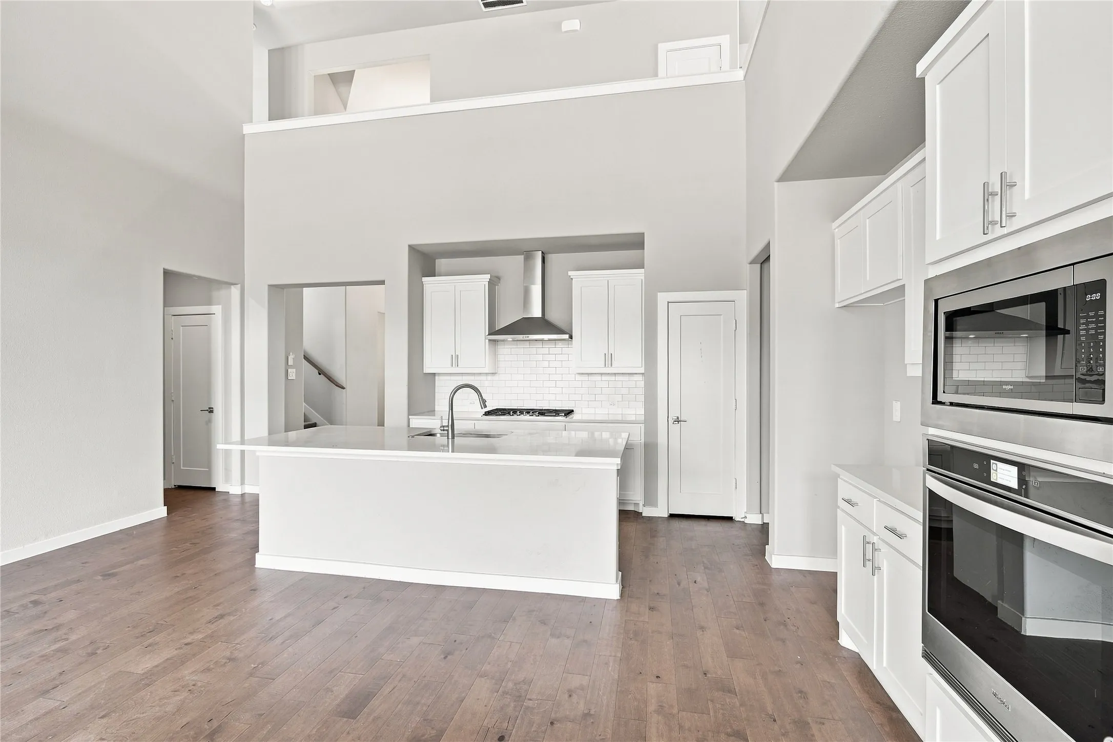 Open-concept kitchen featuring an island with sink, stainless steel appliances, white cabinetry, and wood-finish flooring