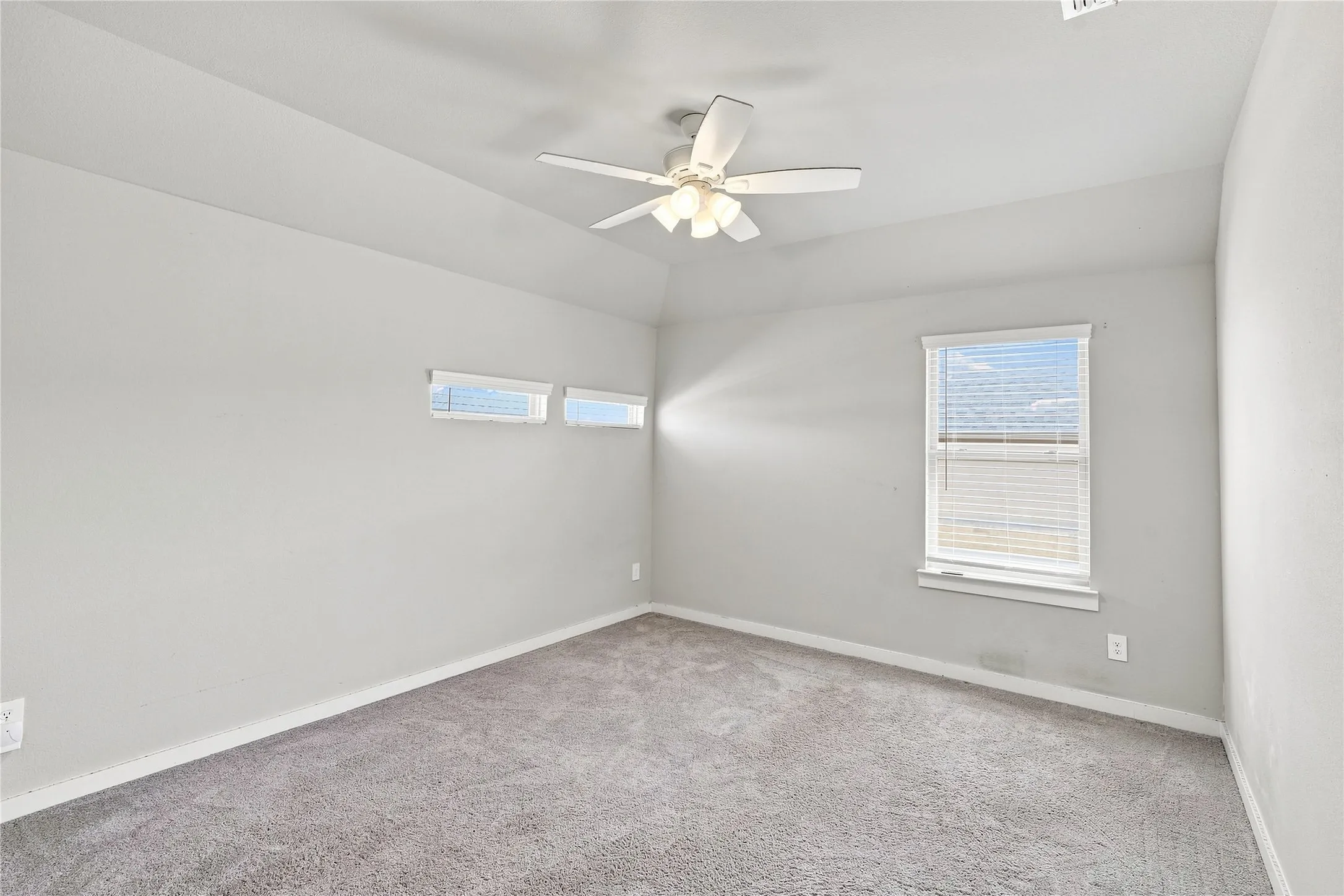 Carpeted flooring with light gray walls, a ceiling fan with integrated lighting, and multiple windows with blinds