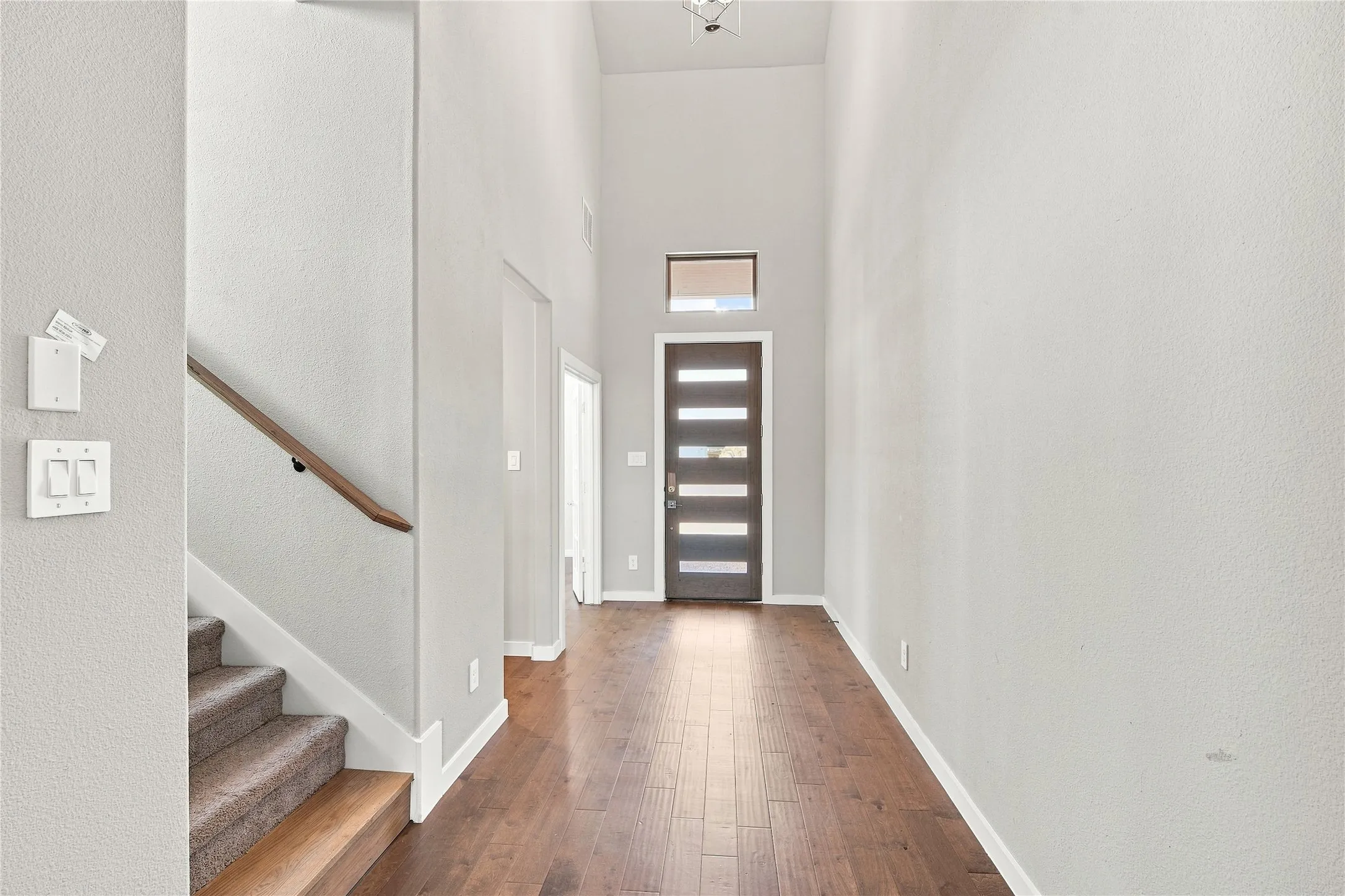 Foyer featuring high ceilings, wood-finish flooring, a contemporary front door with horizontal lites, and a staircase with a wood handrail