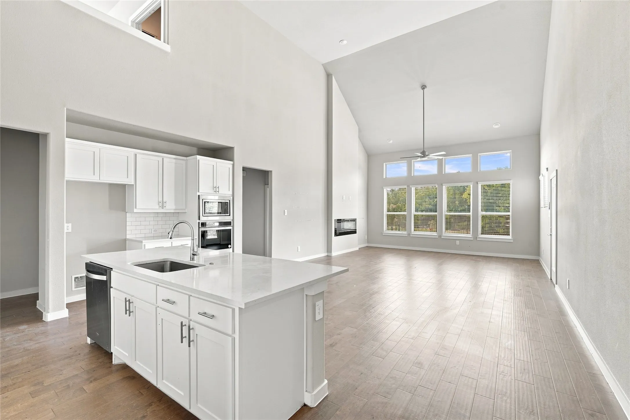 Vaulted ceilings, wood-finish flooring, white shaker cabinetry, an integrated kitchen island with sink, and a modern fireplace