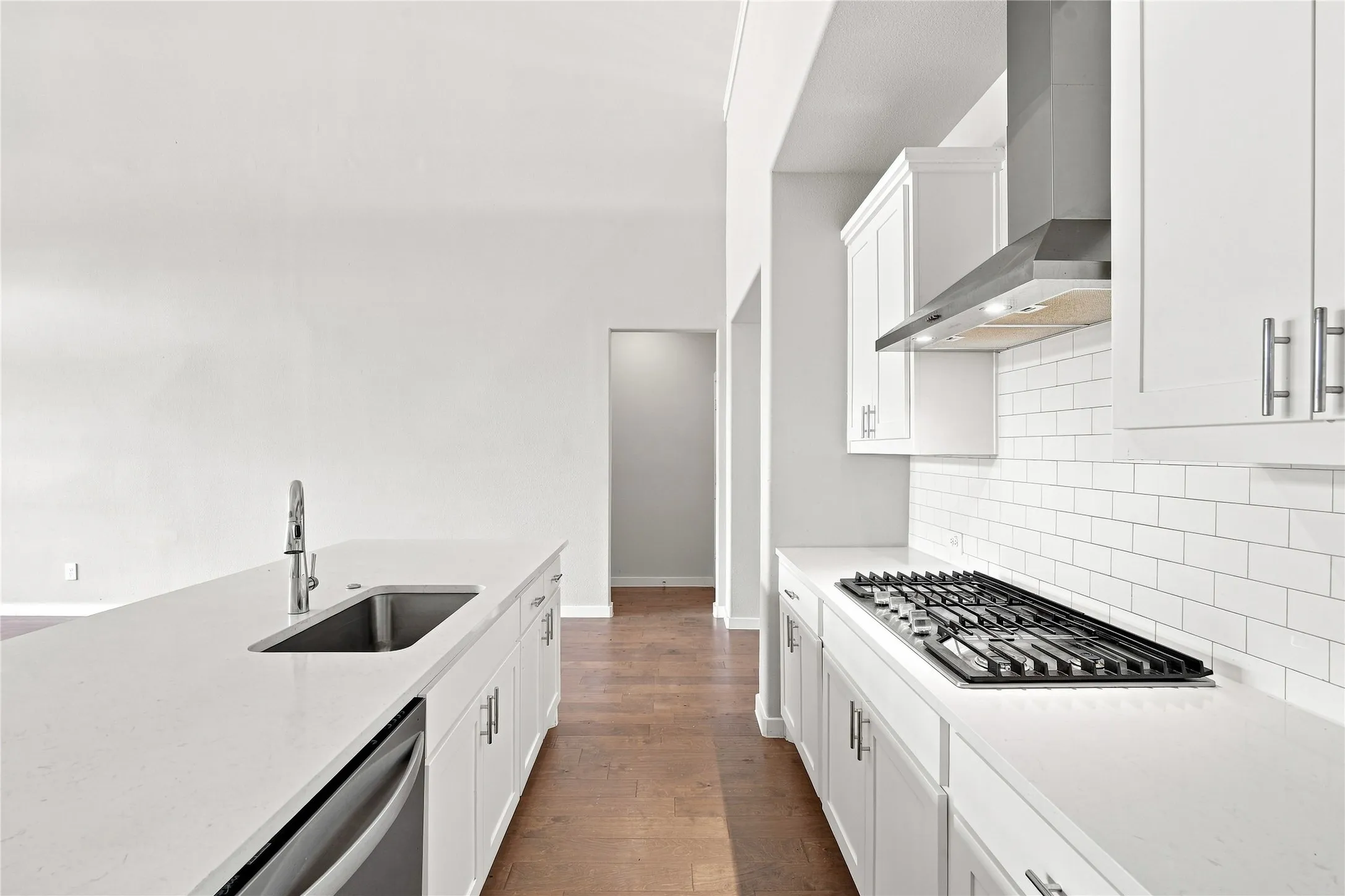 White shaker-style cabinetry, stainless steel appliances, white subway tile backsplash, and wood-finish flooring