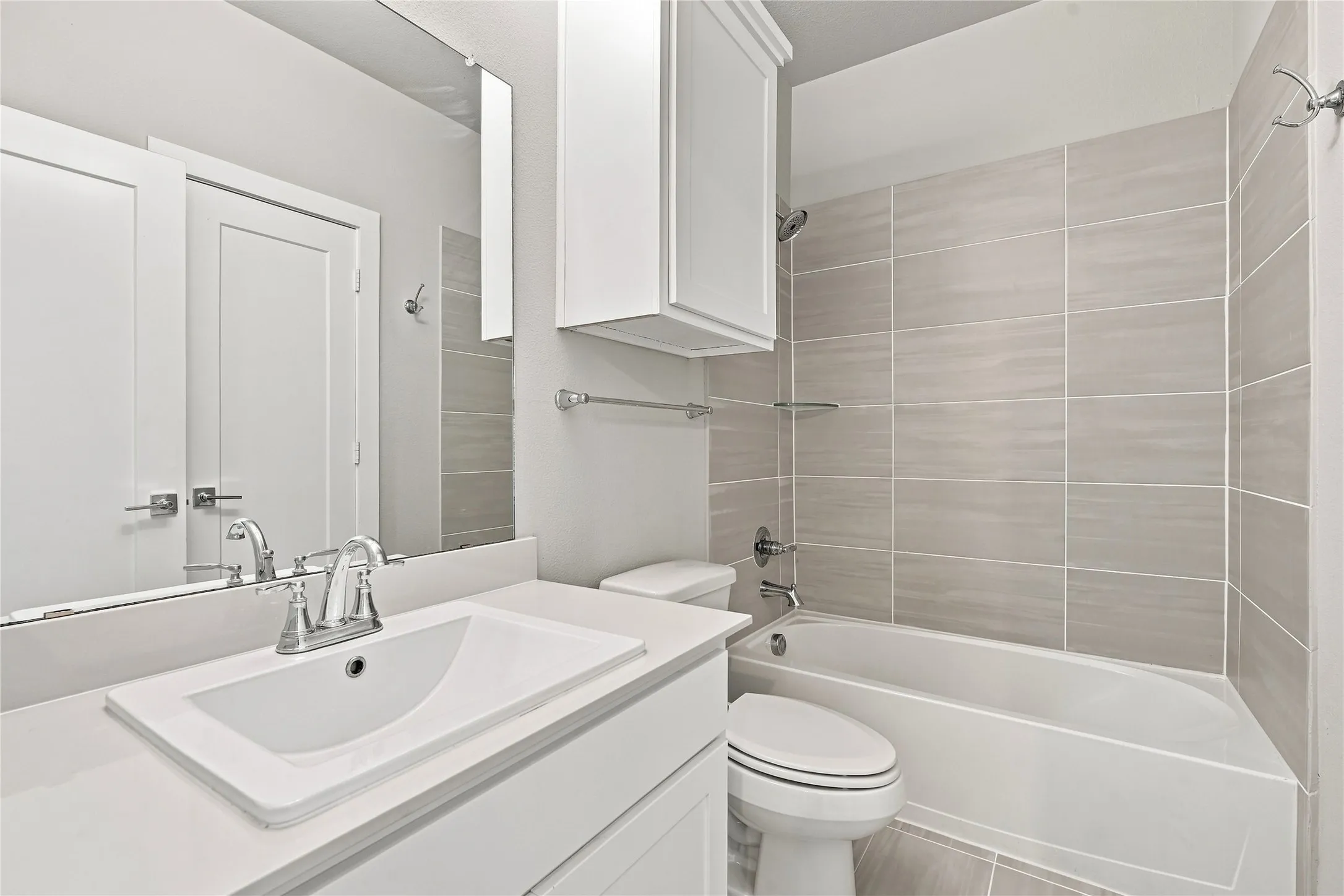 Modern bathroom featuring a single vanity with an undermount sink, a chrome-finish faucet, a built-in wall cabinet, and a tiled tub/shower combination