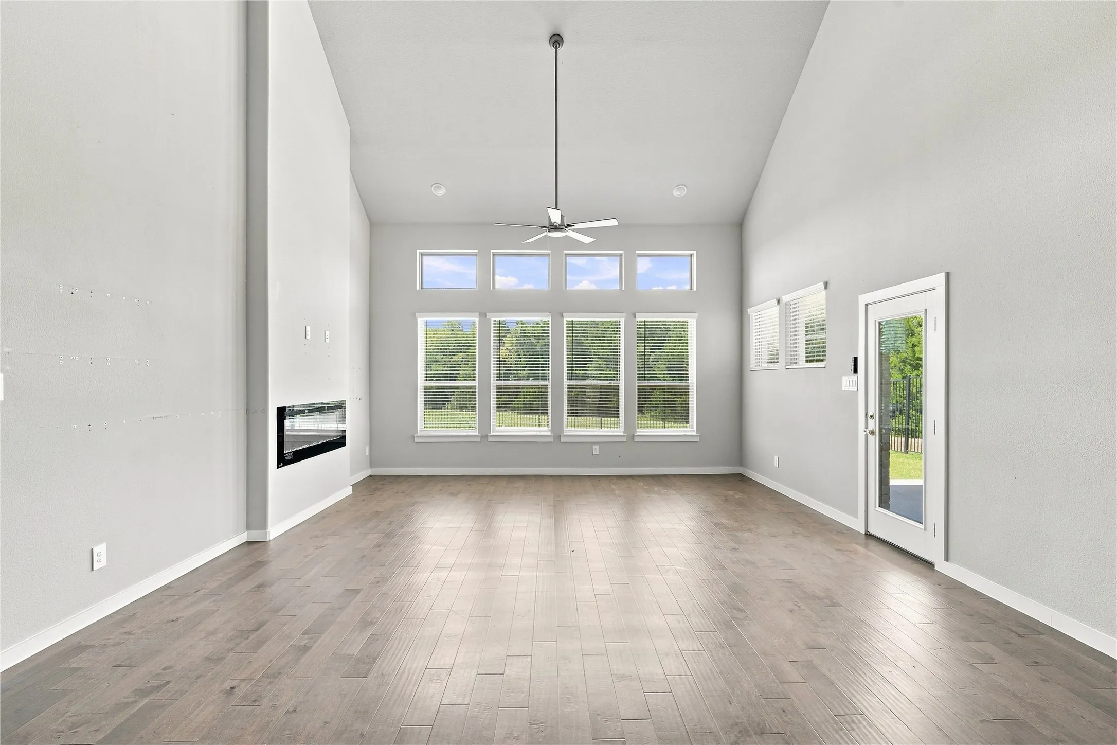 Vaulted ceiling, wood-finish flooring, linear electric fireplace, ceiling fan, and multiple windows