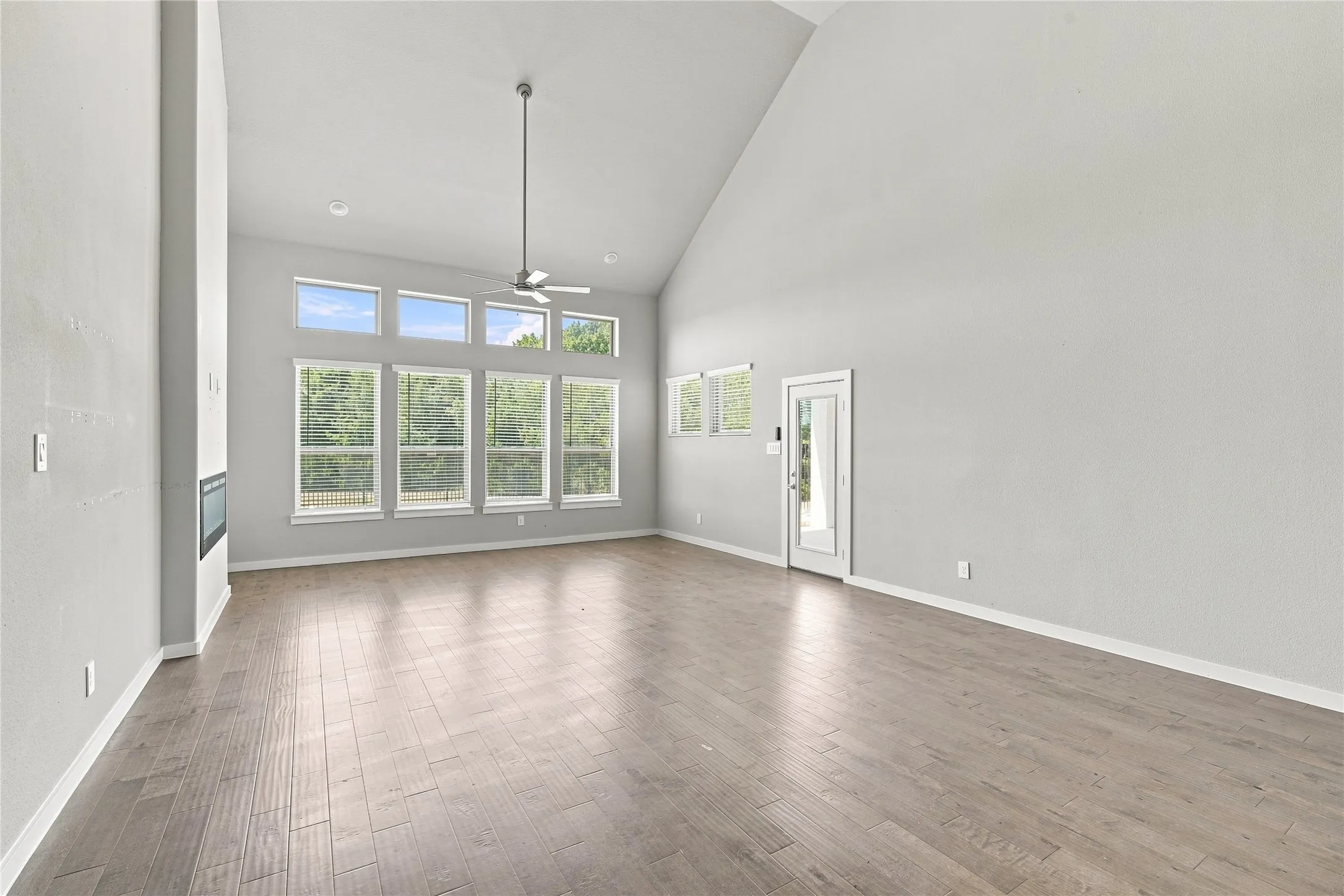Vaulted ceiling great room with wood-finish flooring, a contemporary fireplace, and a full-light exterior door