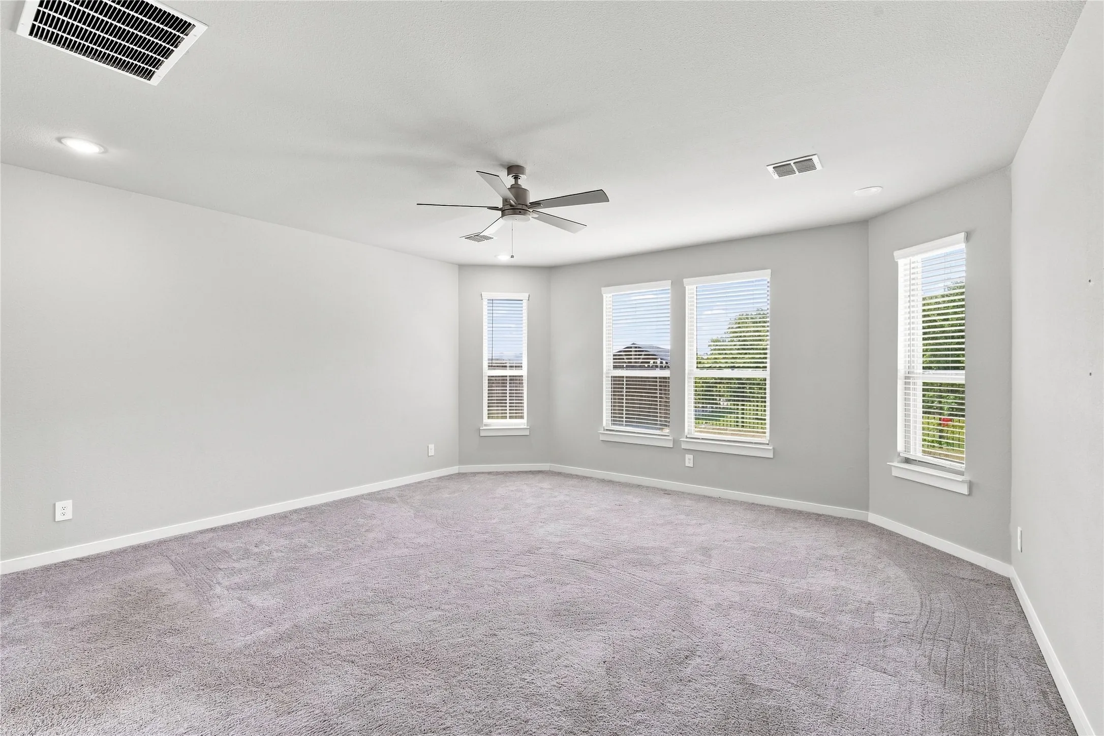 Expansive room featuring light gray carpeting, neutral wall color, recessed lighting, ceiling fan, and multiple windows with blinds