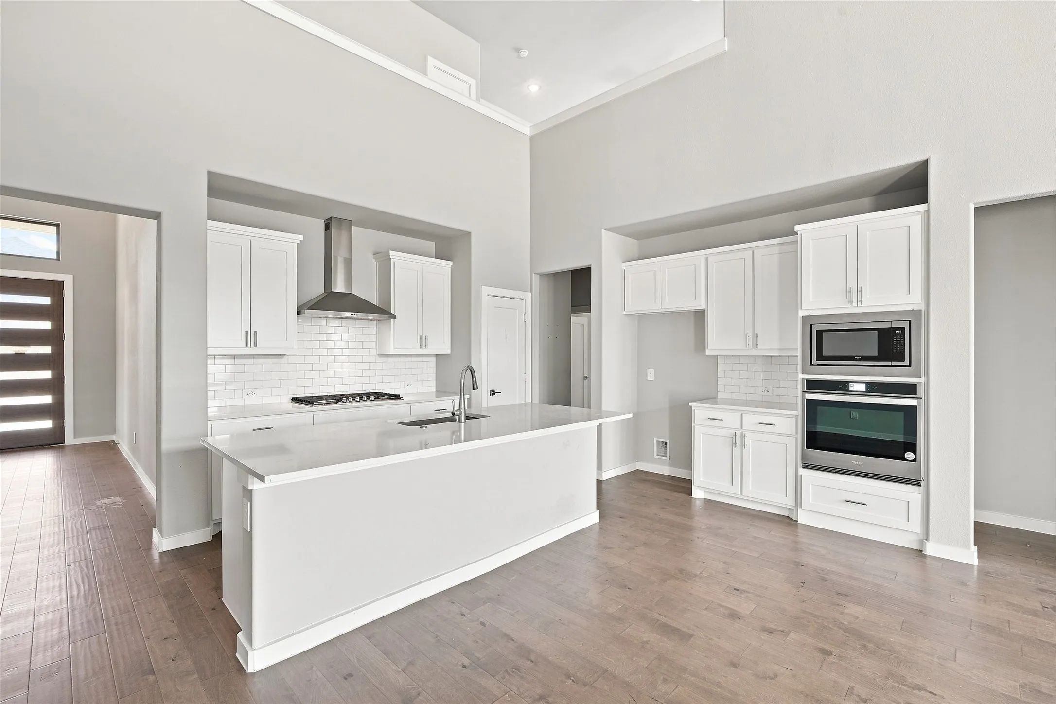 Open-concept kitchen with high ceilings, wood-finish flooring, white cabinetry, a kitchen island, and stainless steel appliances