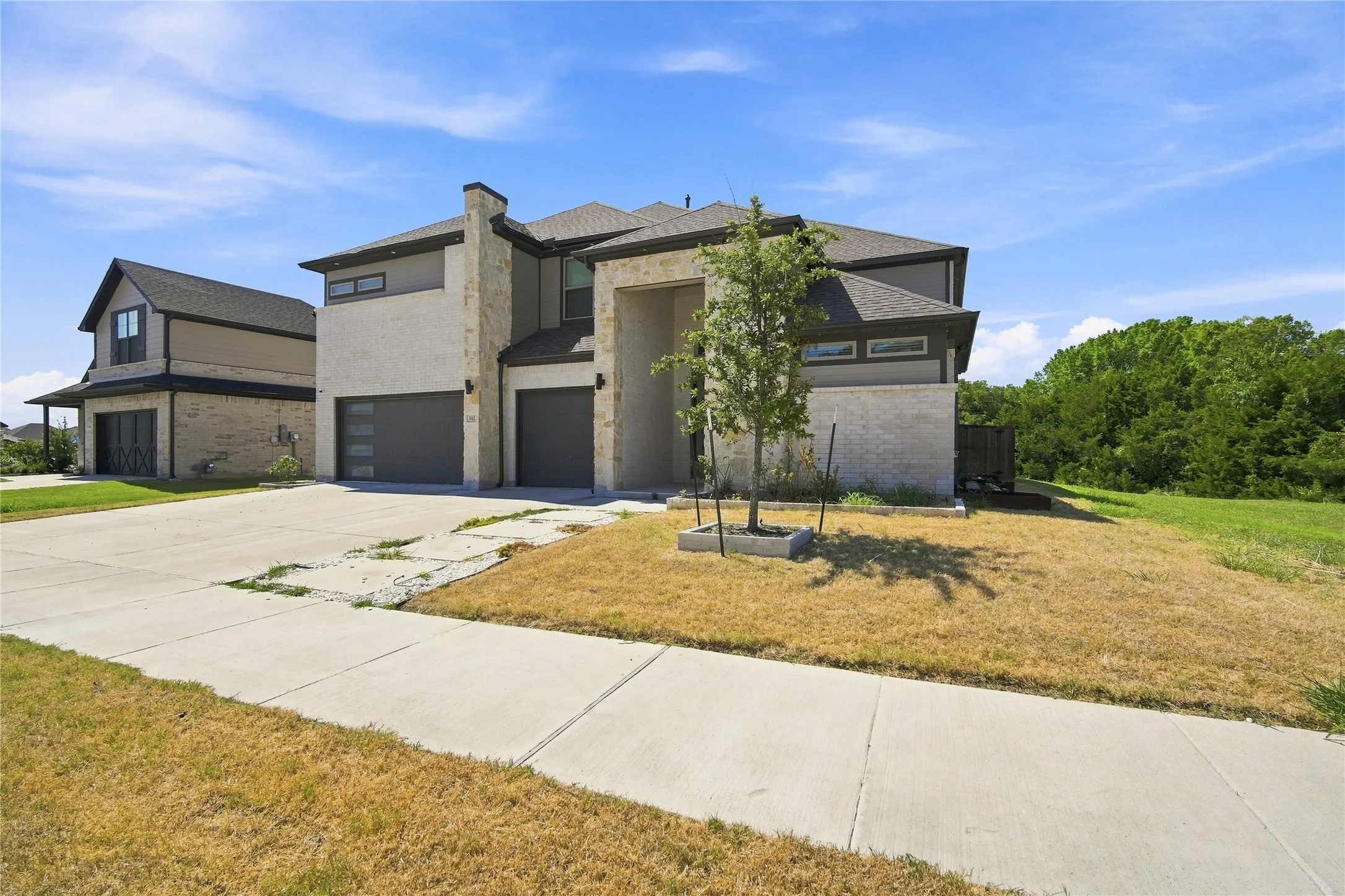 Two-story facade with stone and stucco accents, multiple garage doors, and a concrete driveway