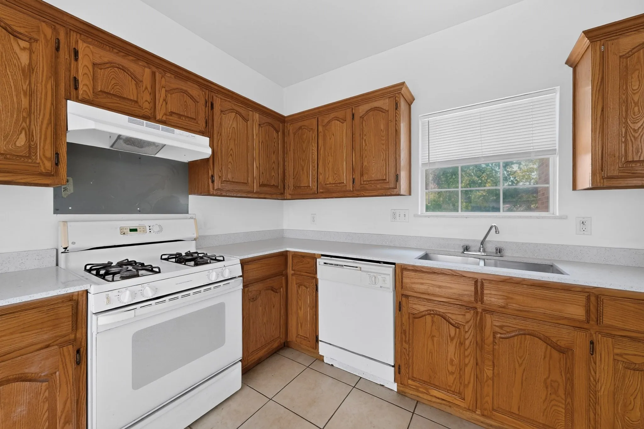 Kitchen featuring wood cabinetry, light-toned countertops, tile flooring, and a window above the sink
