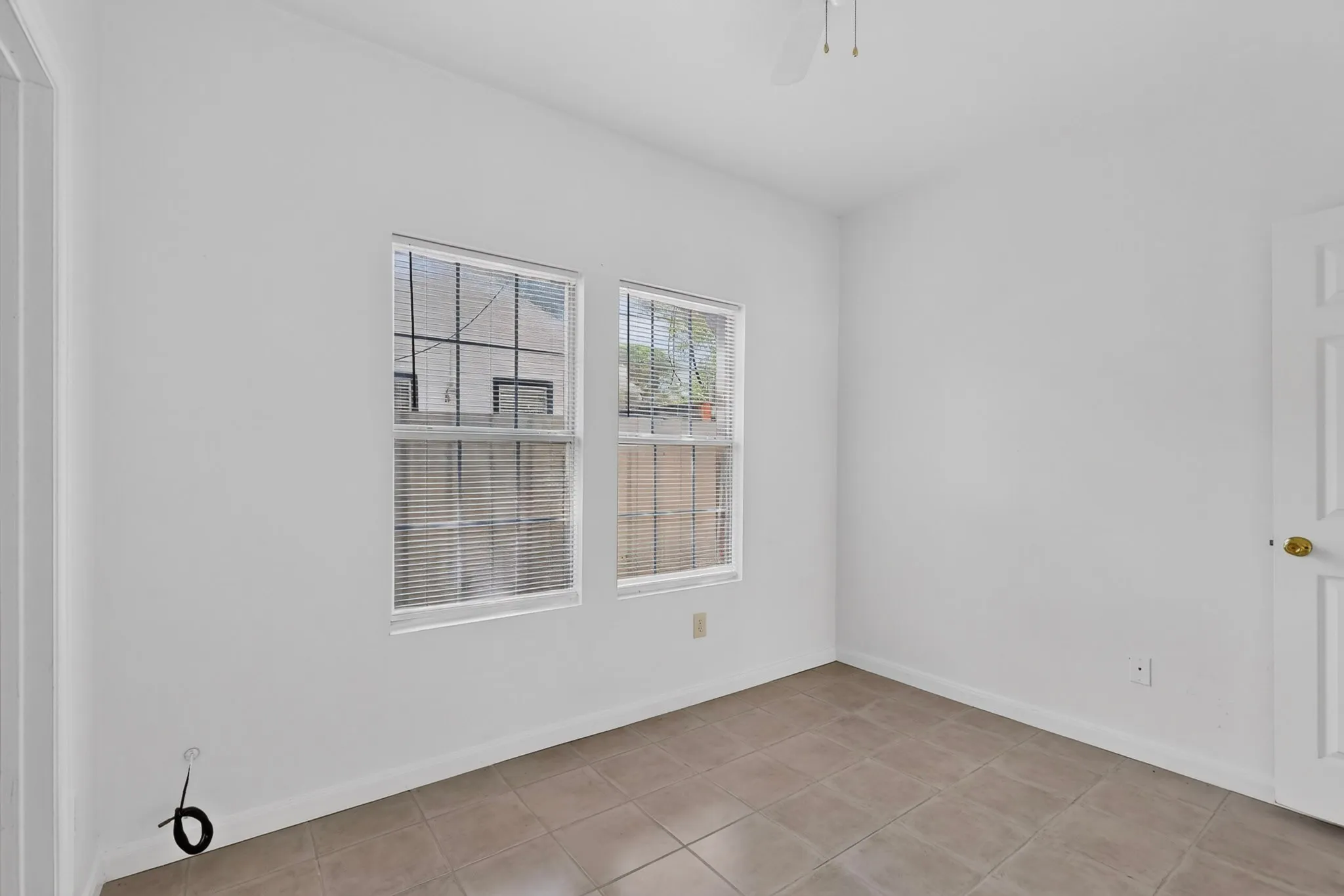Neutral wall paint, tile flooring, two windows with blinds, ceiling fan, and panel door