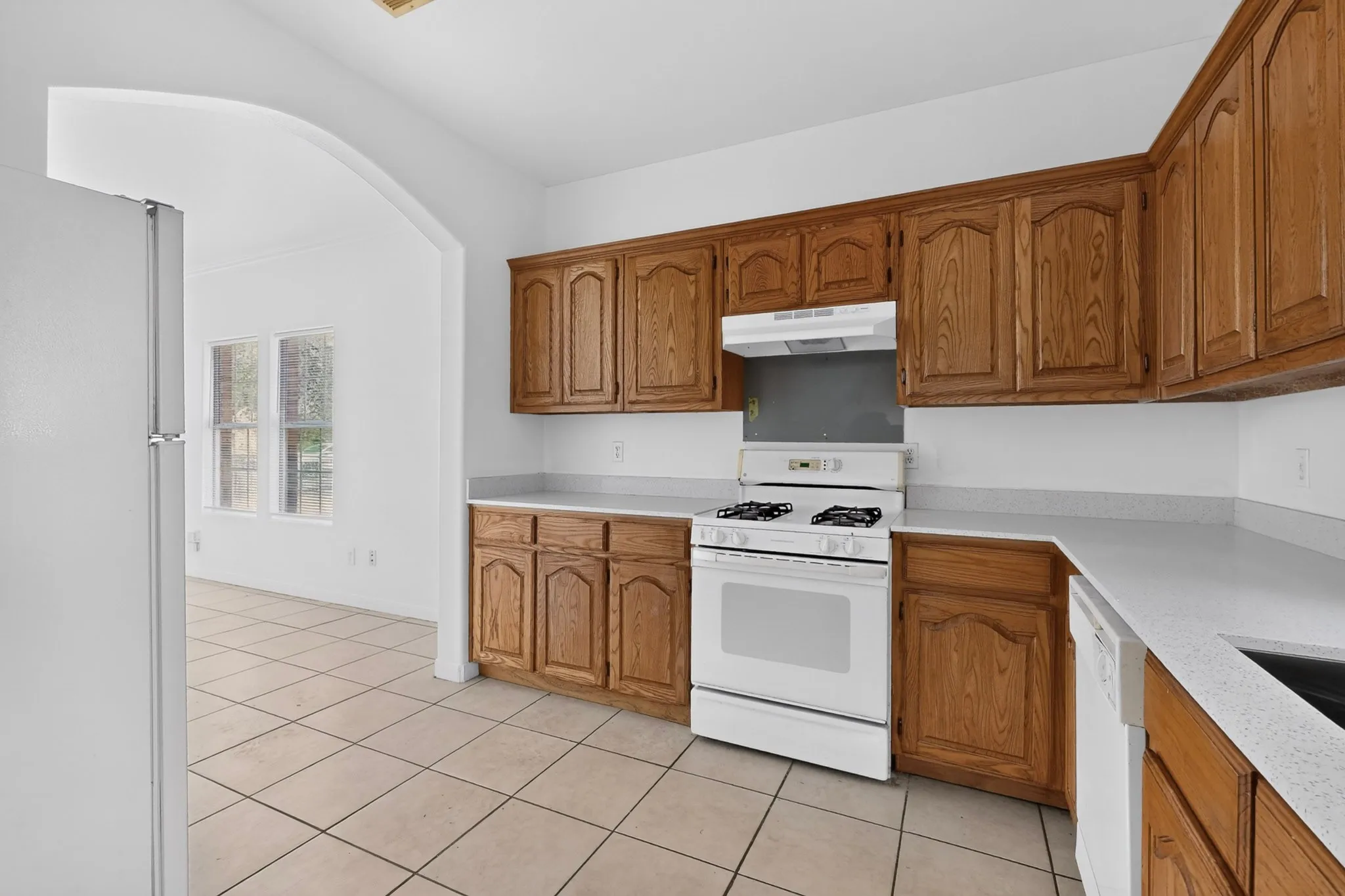 Kitchen with wood cabinetry, light-toned countertops, white appliances, and tiled flooring