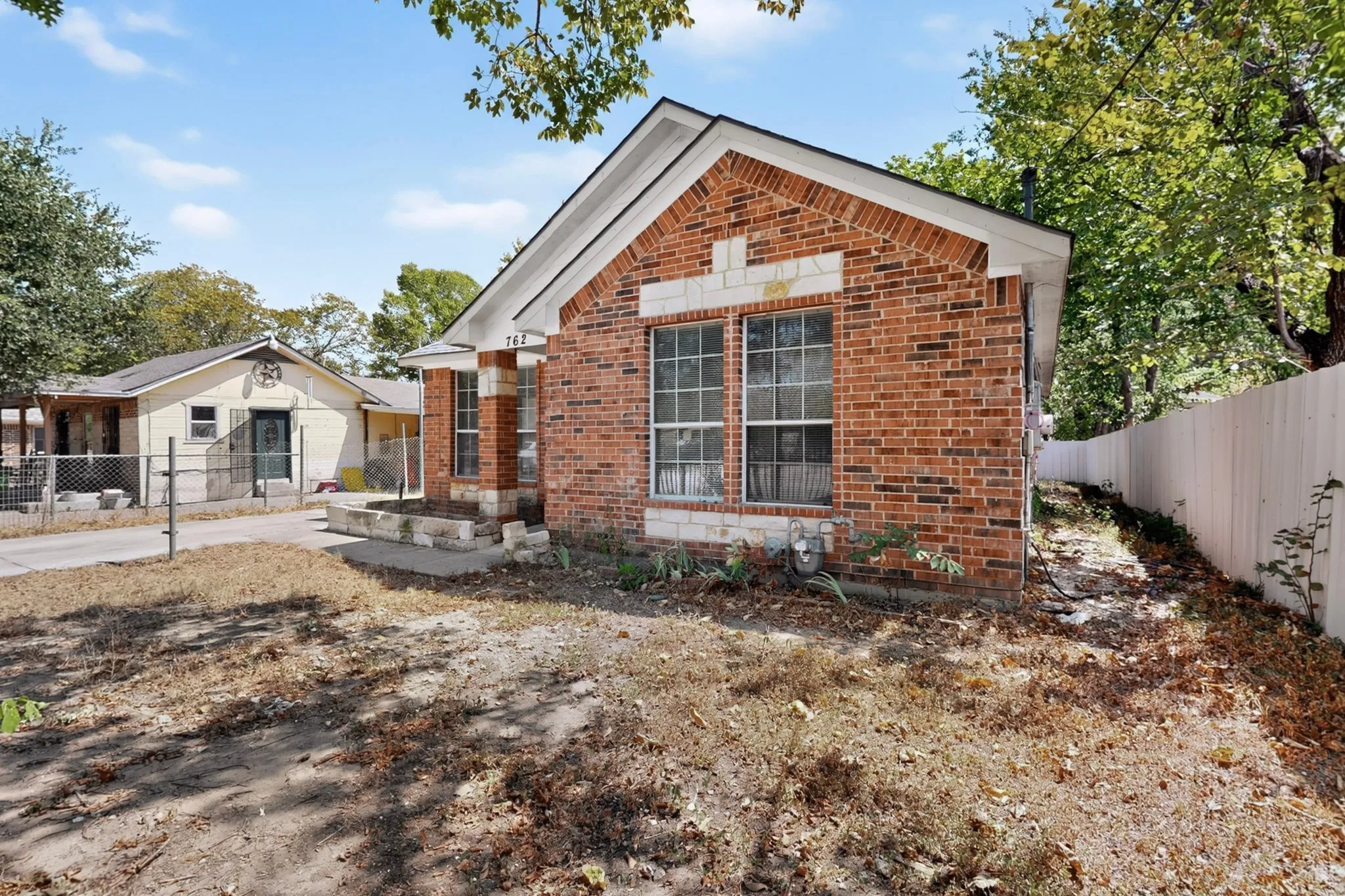 Brick exterior with white trim, featuring a side yard with a white privacy fence