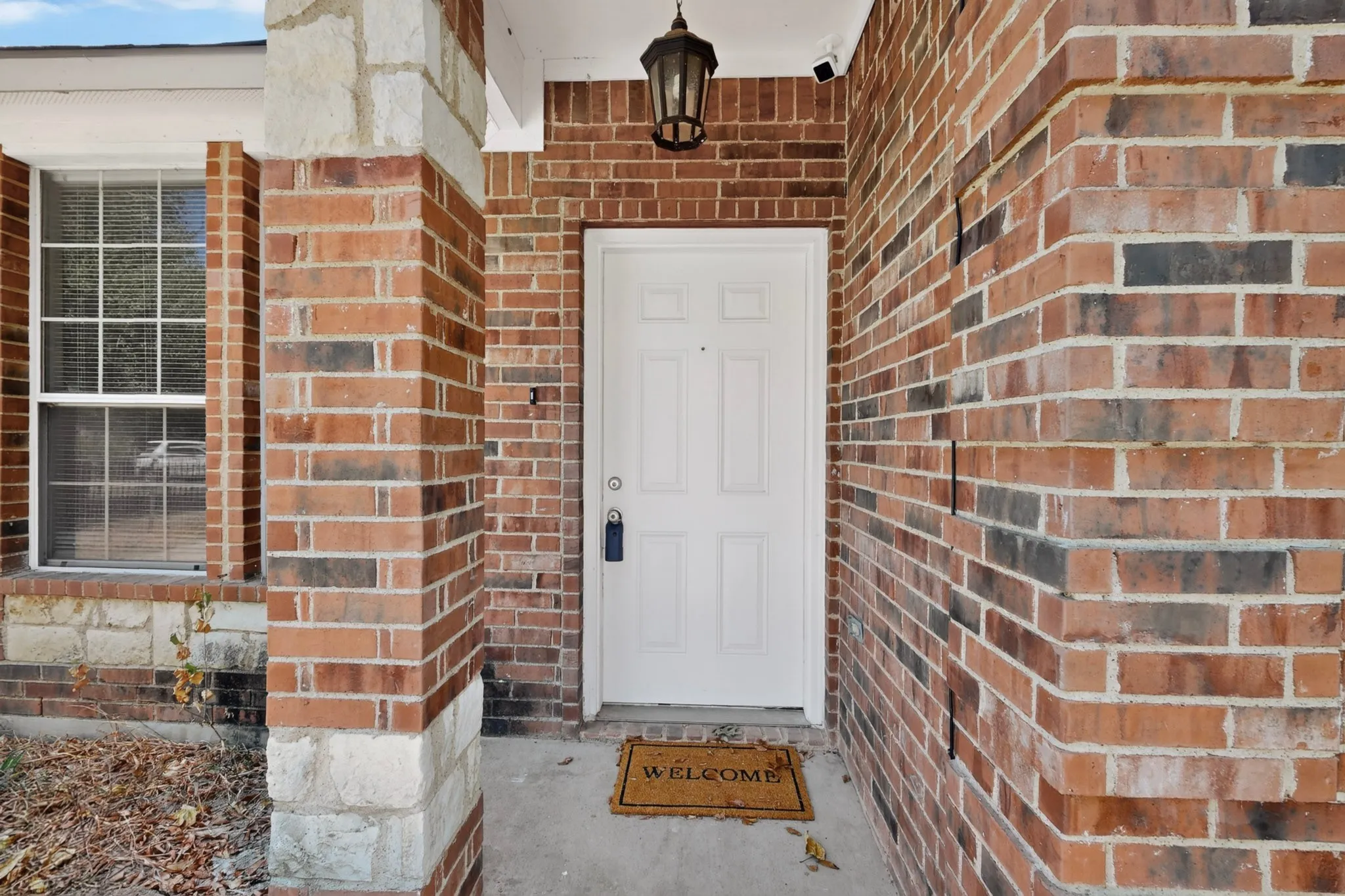 Brick exterior with stone accents, white paneled entry door, and an exterior lantern fixture