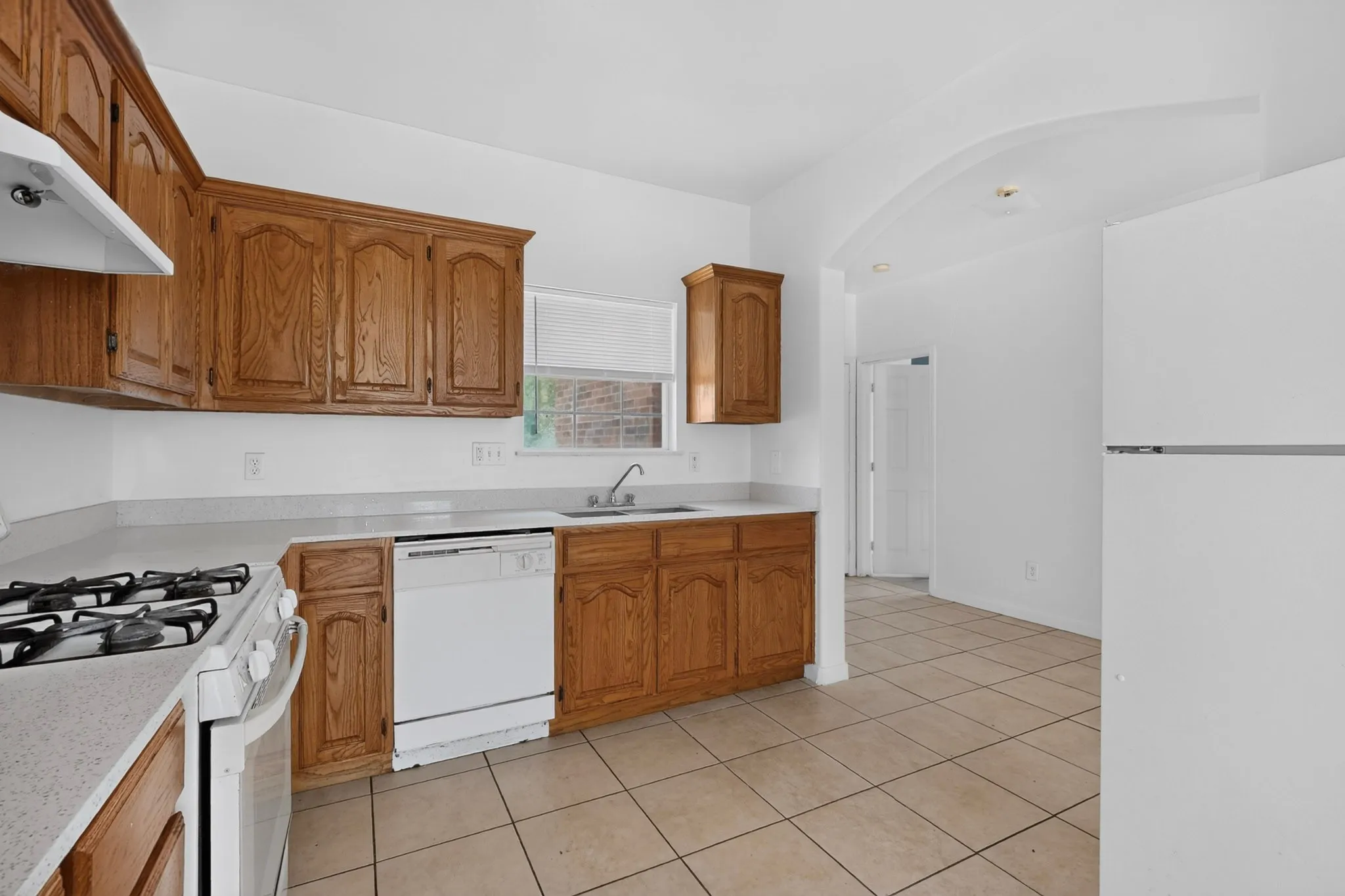 Wood cabinetry, white countertops, built-in dishwasher, gas range, and ceramic tile flooring