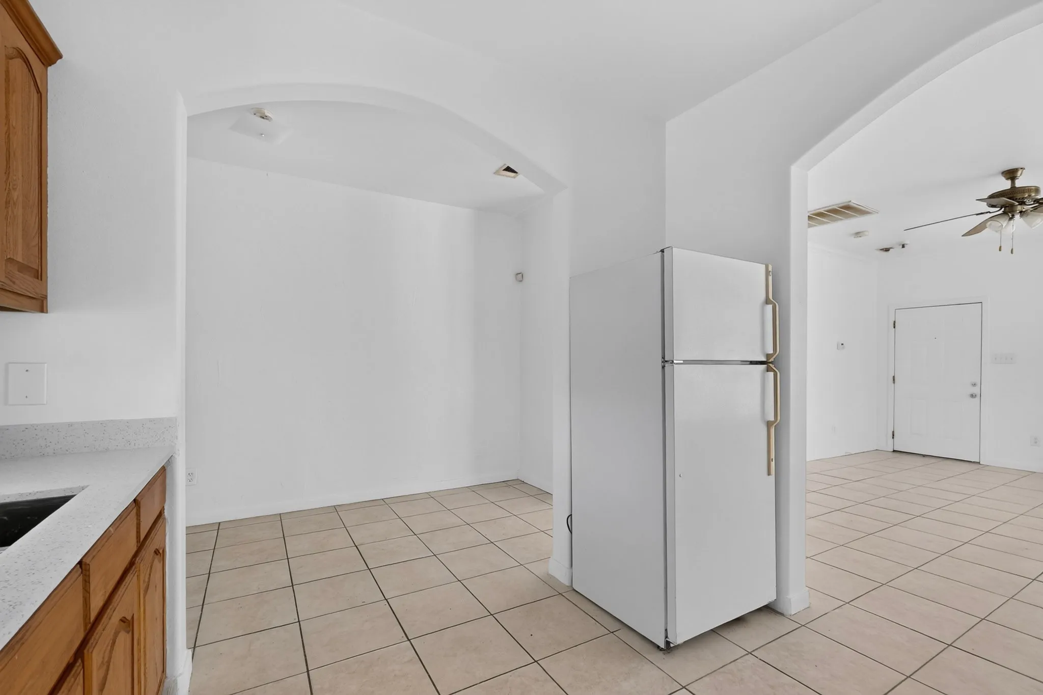 Archways creating distinct areas, tile flooring throughout, wood-finish cabinetry, light-toned countertops, and recessed lighting
