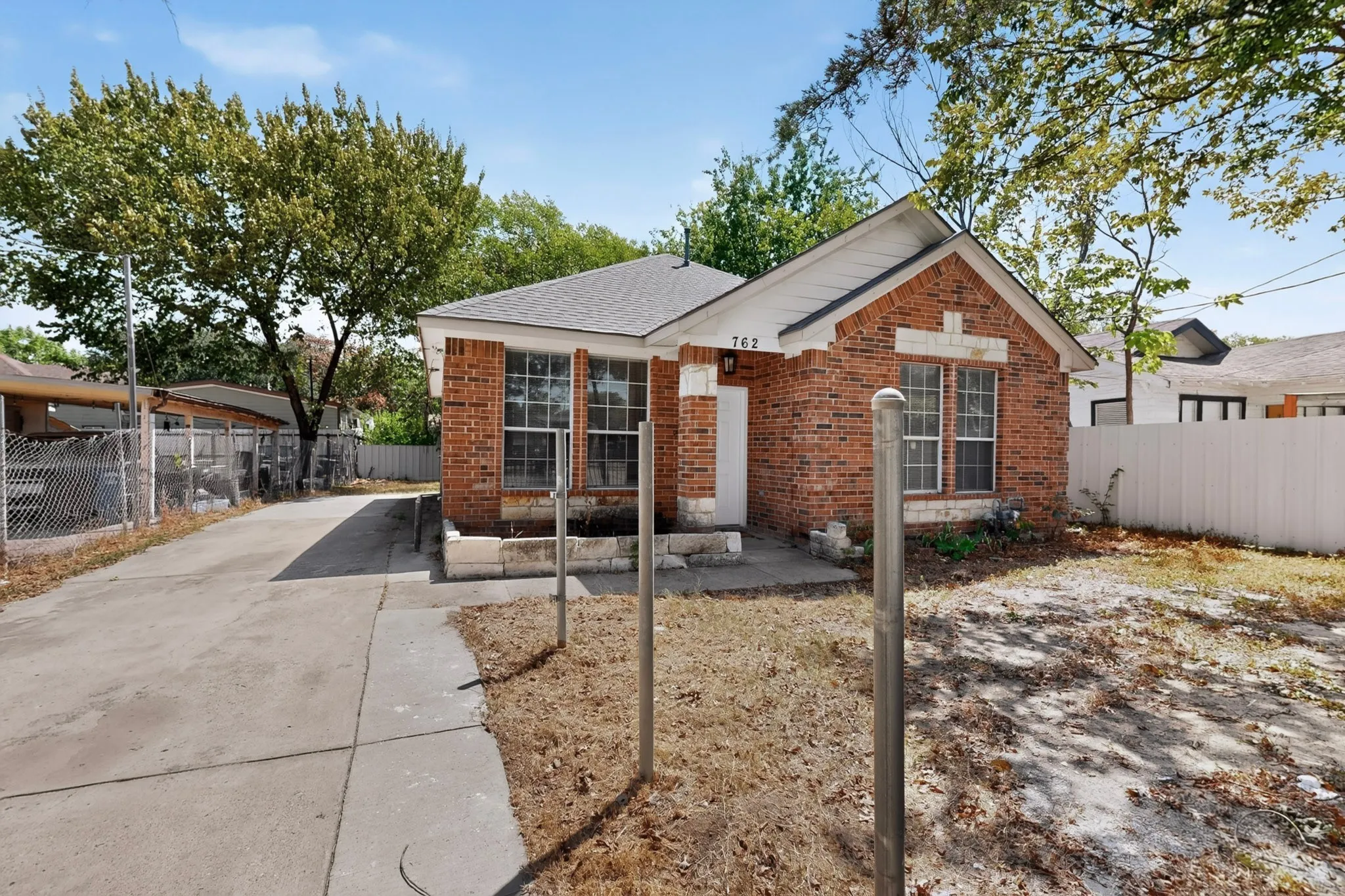 Brick facade residence with a gabled roof, white trim, a concrete driveway, and a chain-link fence