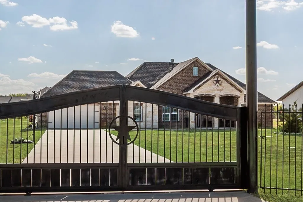 Wrought iron gate with star medallion, brick and stone exterior, multi-gabled roofline, concrete driveway, and manicured lawn