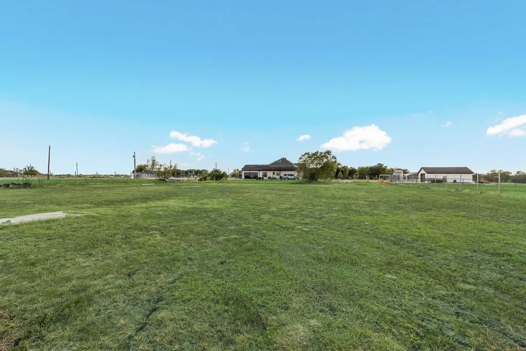 Expansive green space featuring a residence with a dark roof and a separate outbuilding with a dark roof